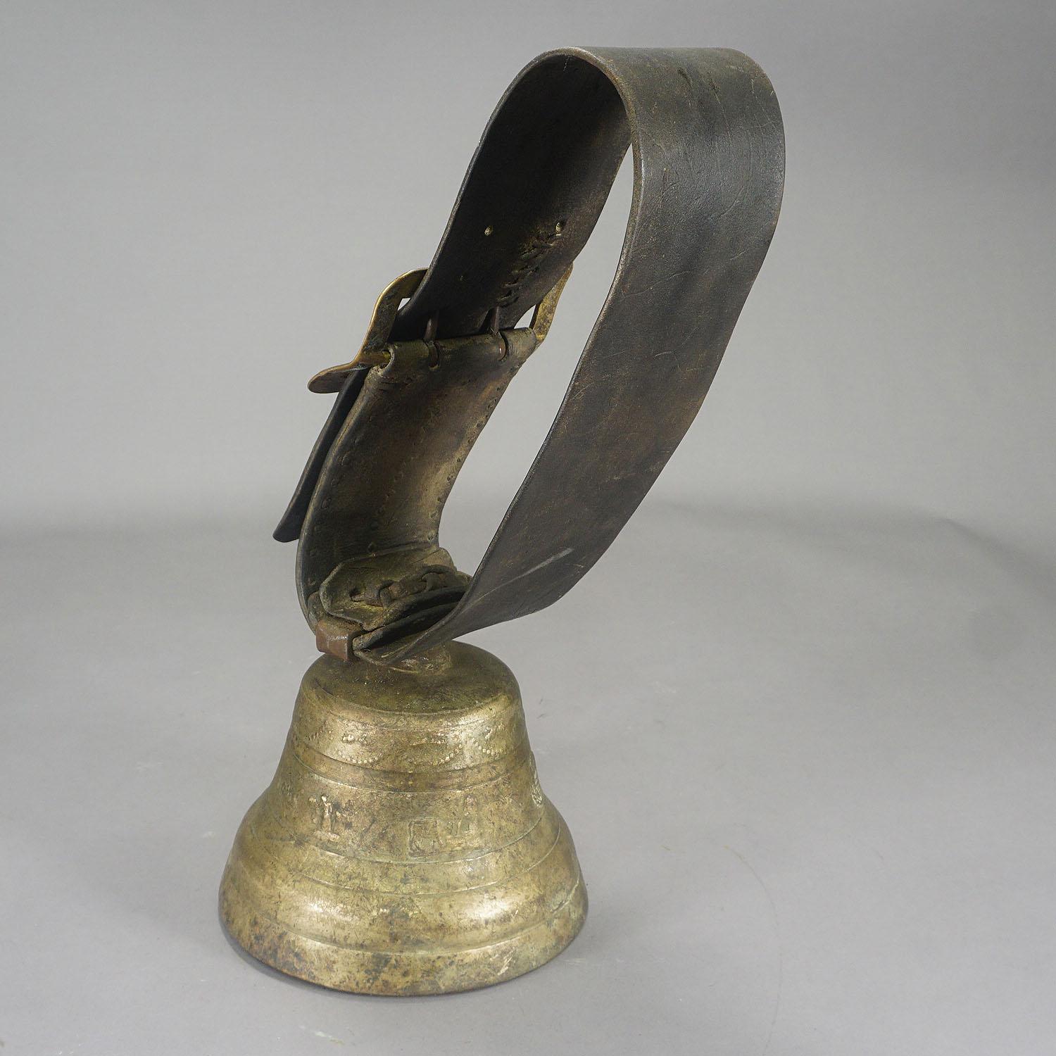 A large casted bronze cow bell from the alps region of Switzerland, manufactured around 1900. The antique bell features high relief motifs of heraldig symbols of Swizerland, cows and farmers. The bell comes with its original brown leather strap with