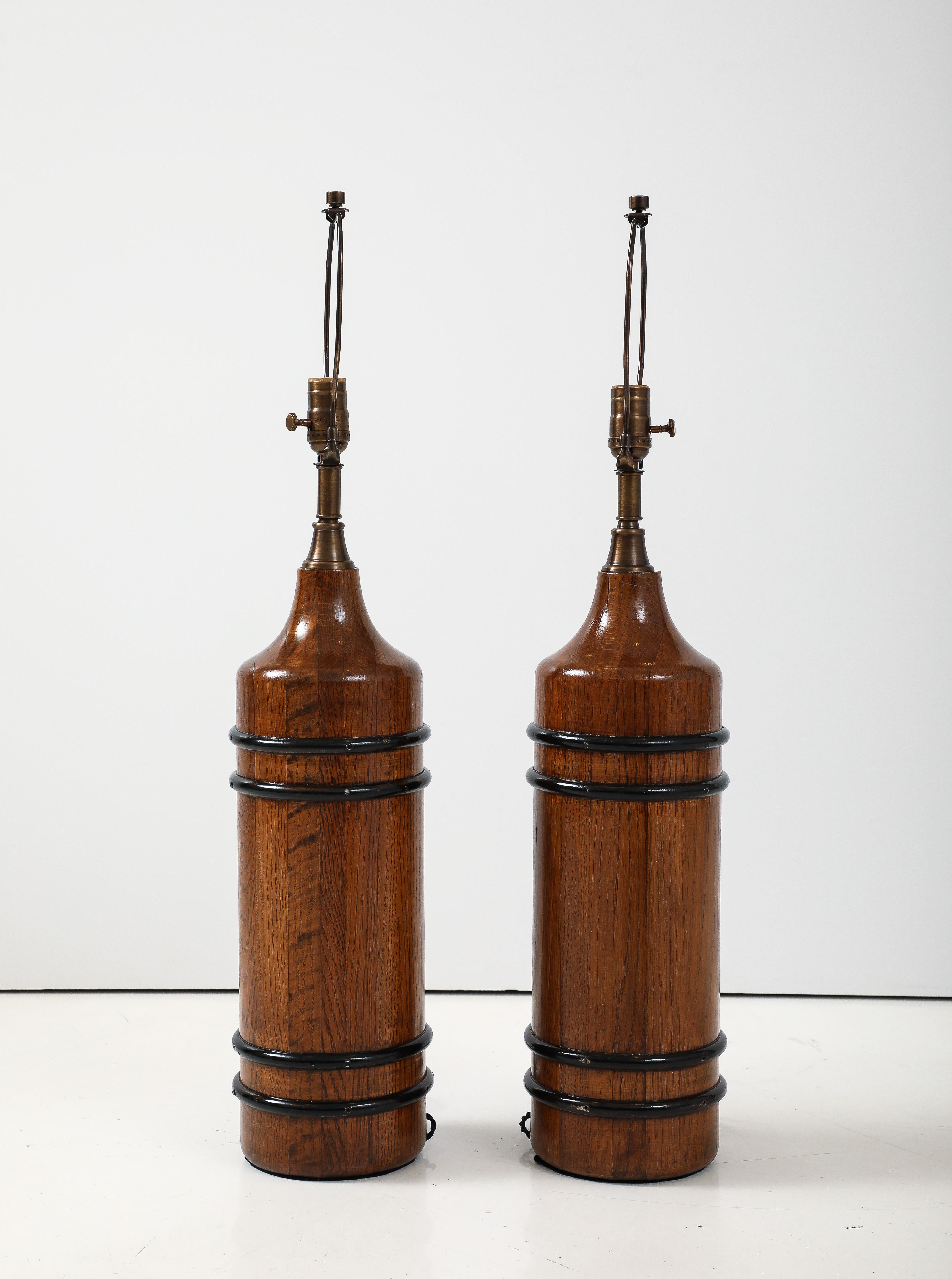 Pareja de lámparas en forma de botella monolítica de pino macizo con acabado al aceite frotado a mano y bandas de hierro ennegrecido. Recableado para su uso en EE.UU. por un electricista homologado por UL, utilizando tomas de corriente, enchufes y