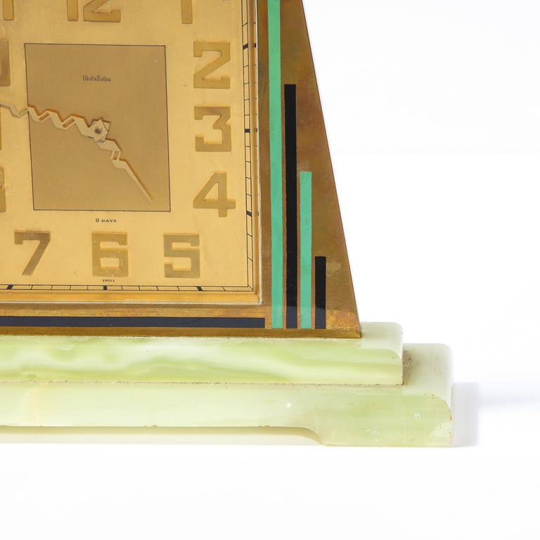 This exquisite Art Deco Machine Age clock was realized in Switzerland by the esteemed jewelry company Udall and Ballou circa 1935. It features a rhombus form brass body with black and celadon skyscraper style detailing; iconically Art Deco numbers