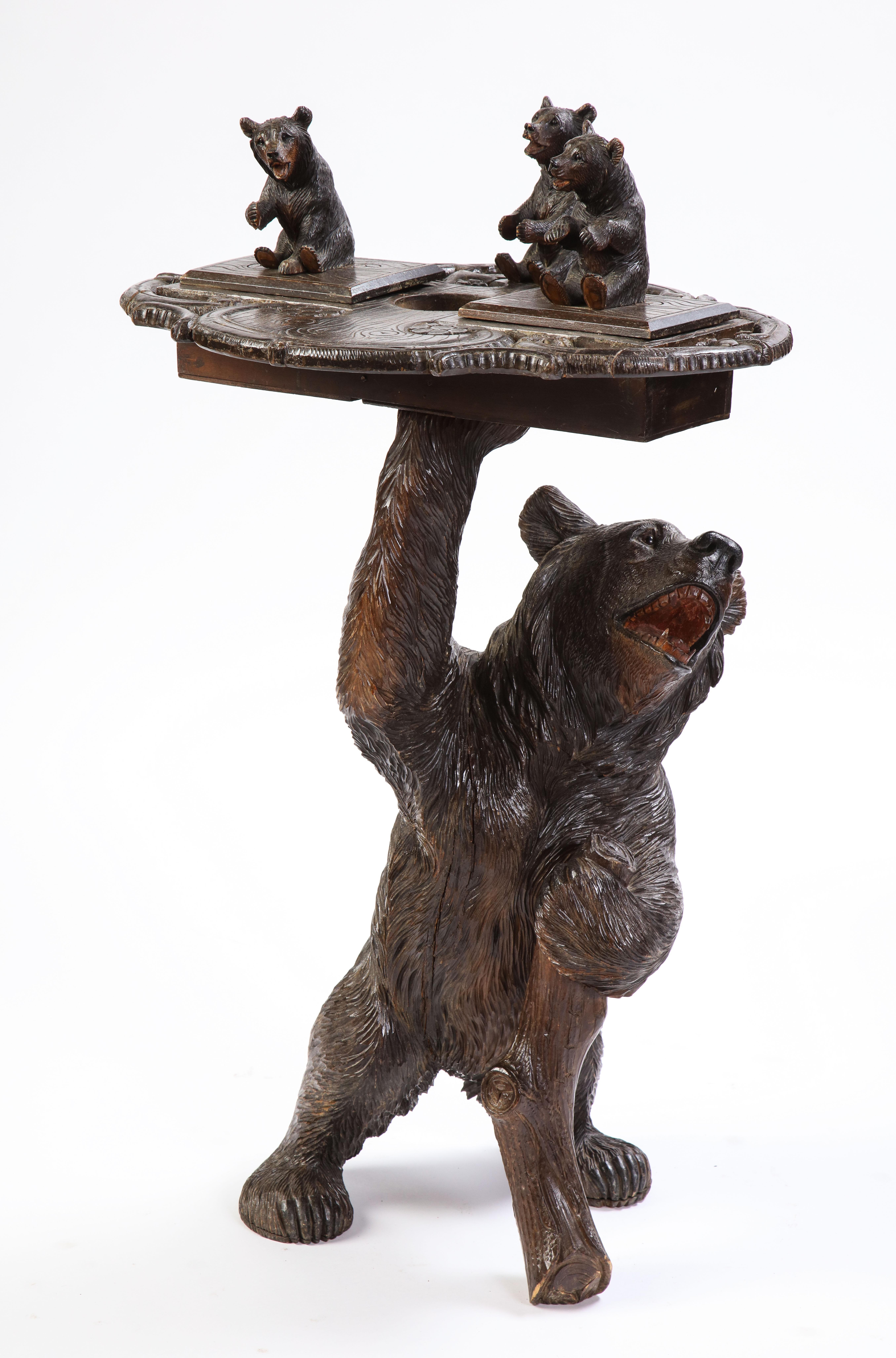 Swiss 'Black Forest' smoking stand, early 20th century. An oval pierced top with two hinged tobacco wells and three seated bears, below the naturalistic column, supported by a standing bear with a hinged head. 

The table's standard is in the form