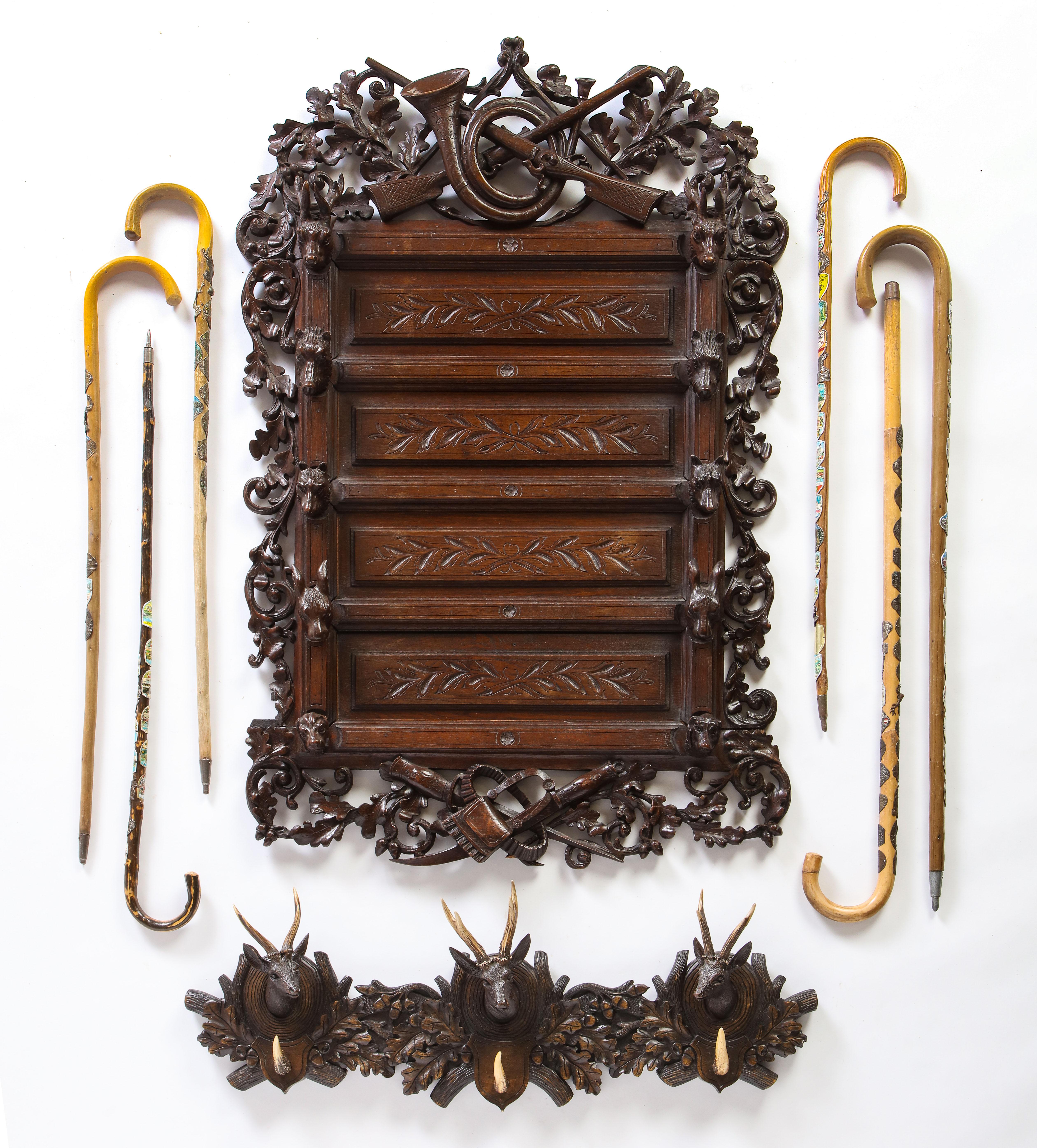 A stately Swiss ‘Black Forest’ wall-mounted walking stick stand dated to the mid-20th century is presented together with six walking sticks, and a Swiss 'Black Forest' carved wood and antler-mounted hanging coat rack. The carved wood decorations on