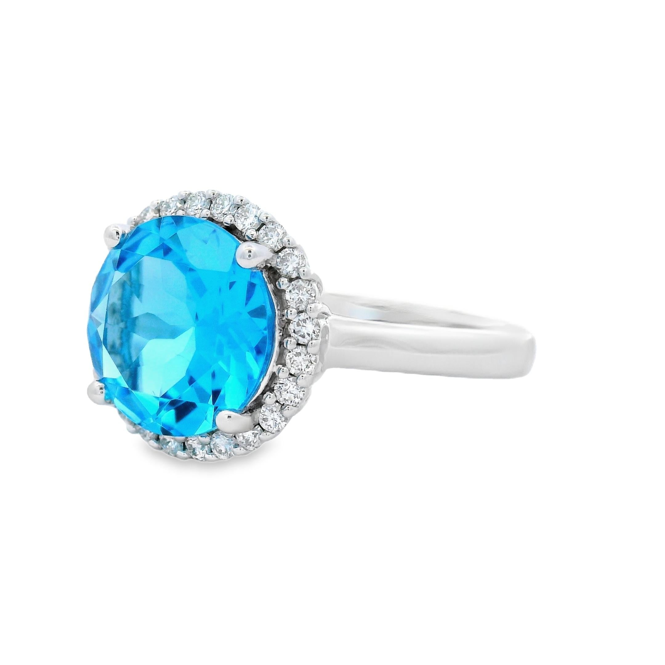 Cette bague de cocktail aux couleurs et à la brillance éclatantes est ornée d'une topaze bleue suisse ronde de 3,90 carats mesurant 10 mm, entourée d'un halo de diamants naturels. La teinte vive et océanique de la pierre centrale est accentuée par