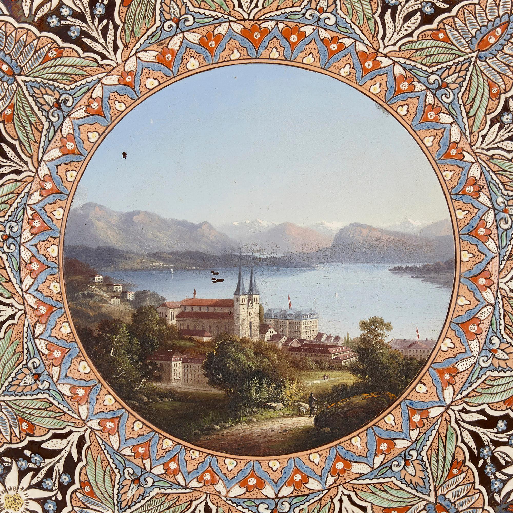 Swiss charger-shaped faience plaque depicting a lakeside chateau
Swiss, late 19th century
Measures: Frame: Depth 7cm, diameter 50cm
Plaque: Depth 4cm, diameter 39cm

This beautiful framed faience charger is superbly decorated with a variety of