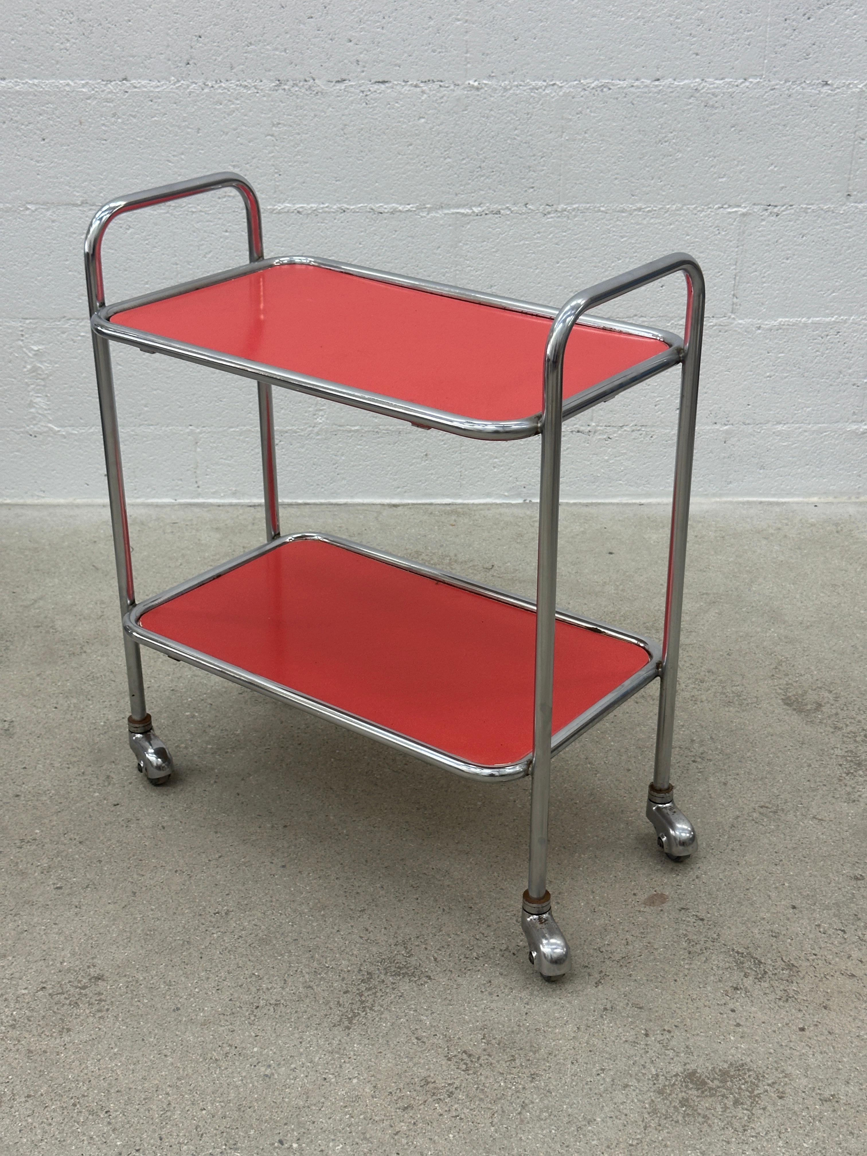 Chariot de bar tubulaire Swiss Design/One avec plateaux en formica rouge

Apportez une touche design à votre intérieur avec ce superbe chariot de service des années 1960.
Son cadre tubulaire et ses plateaux en Formica rouge vif lui confèrent un