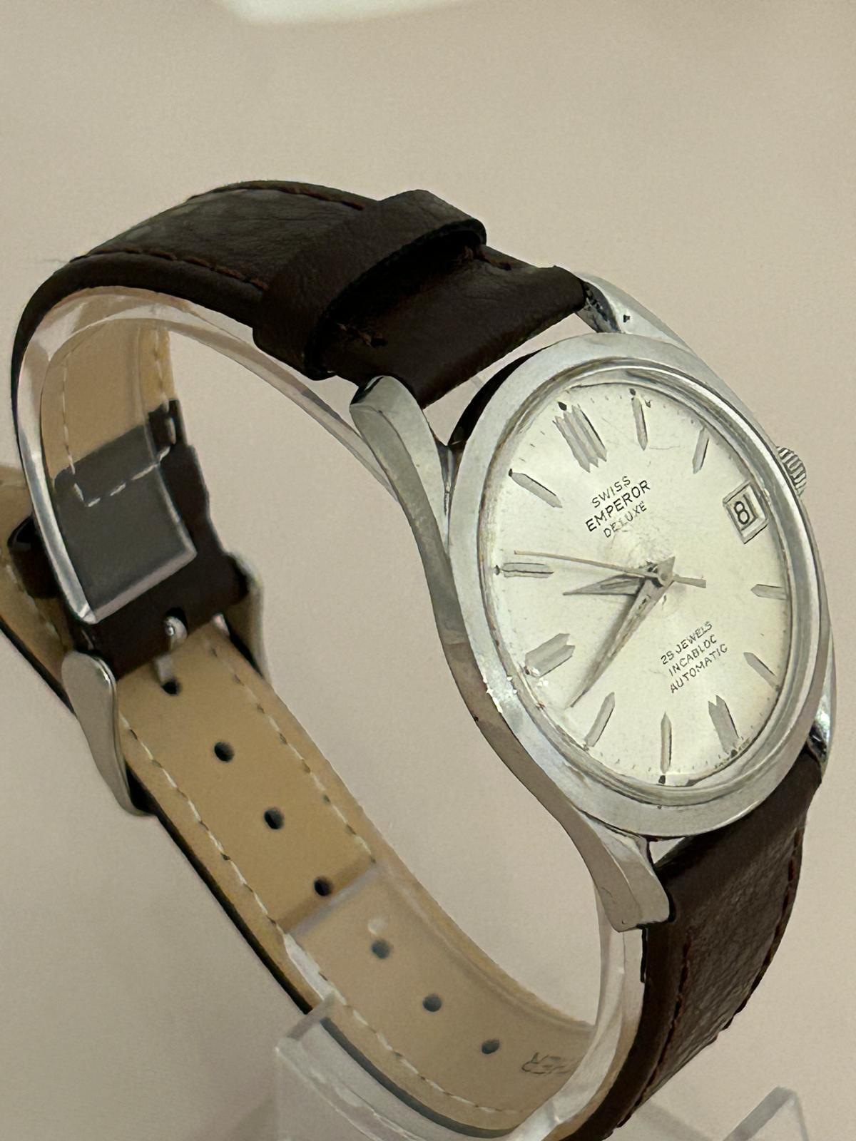 Unsere schöne Swiss Emperor Deluxe, verfügt über ein 35mm (37mm inkl. Krone) Edelstahlgehäuse, mit silbernem Zifferblatt und silbernen Schlagstöcken, angetrieben von einem 23-Juwelen-Automatikwerk mit Datumsfunktion, und ist in sehr gutem Zustand