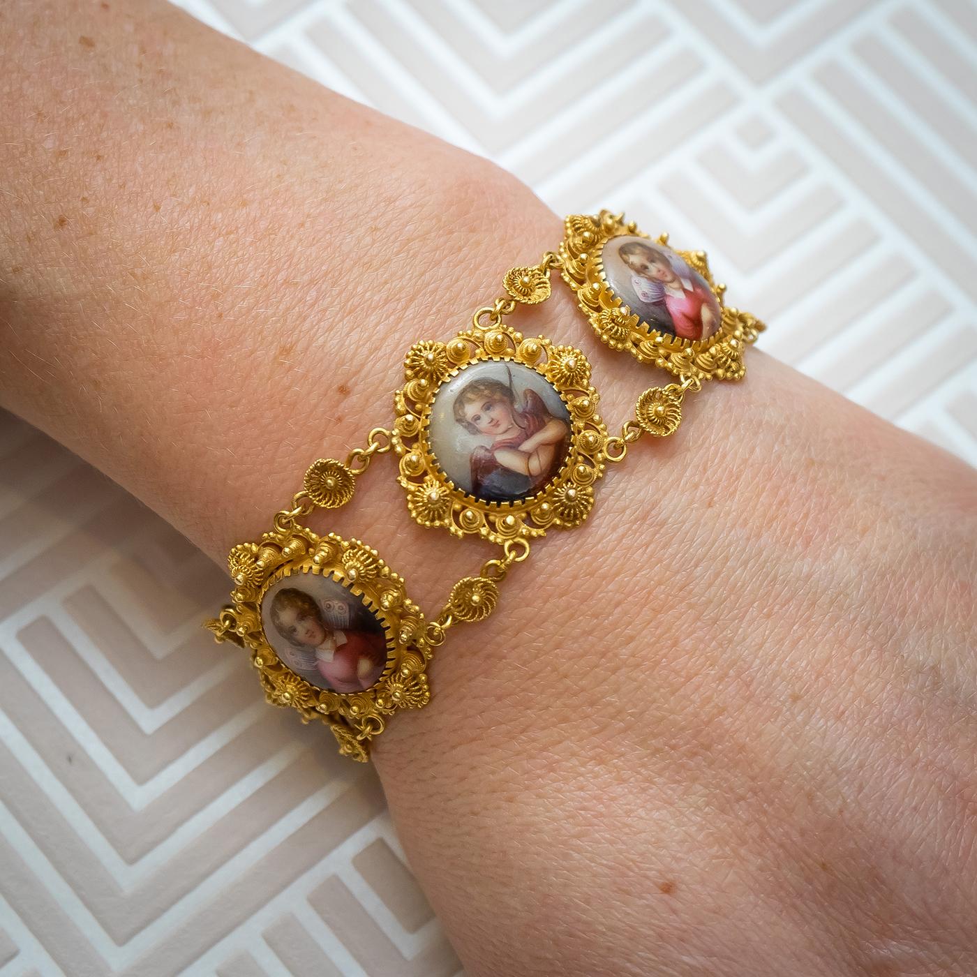 A Swiss enamel cannetille bracelet and pendant suite, with cupid and cherub Swiss enamel plaques, in cannetille gold work, featuring girls in pink dresses, with white collars, with pink and white wings and boys in red togas, with a bow and feather