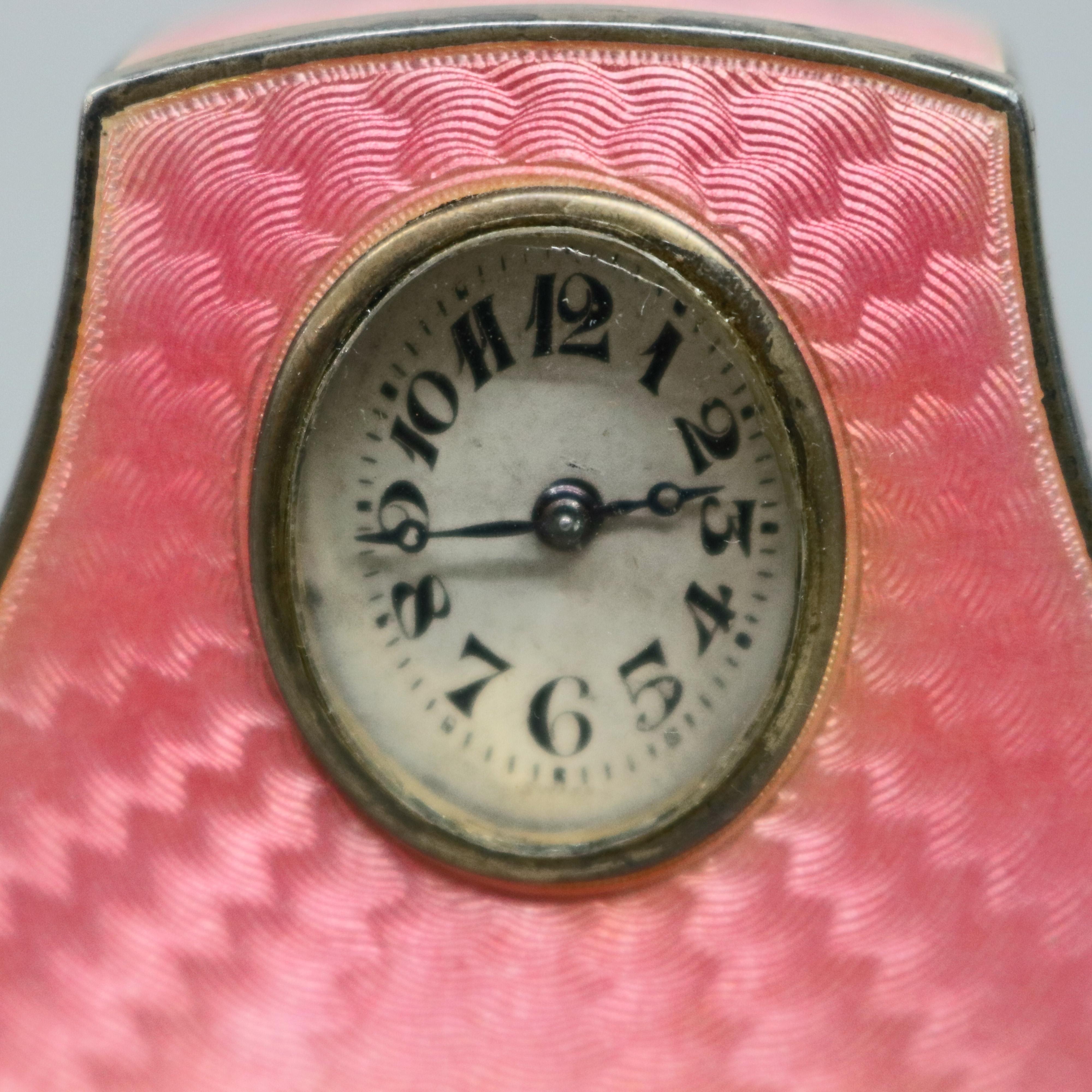 An antique Swiss Faberge School travel clock by Haas Neveux offers miniature camel back clock with pink Guilloche enamel on sterling silver in machined patterning with face having Arabic numbers, drop back case with maker mark on base as