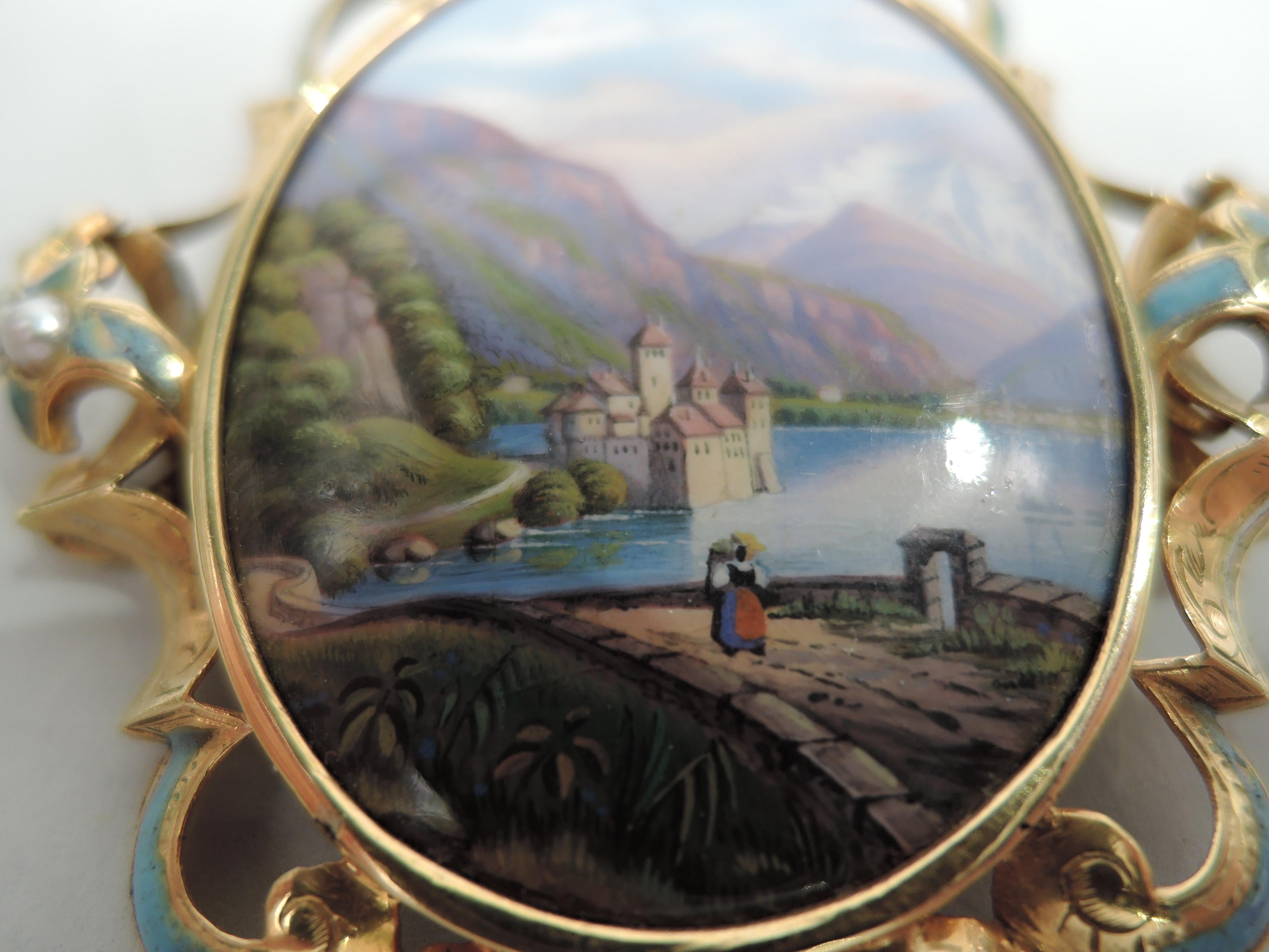 Swiss brooch, ca 1880. Oval enameled plaque in gold frame; rim comprises applied scrolls heightened with enamel and inset with pearls.The plaque depicts the Château de Chillon, a medieval castle set on an island in Lake Geneva, with Mont Blanc in