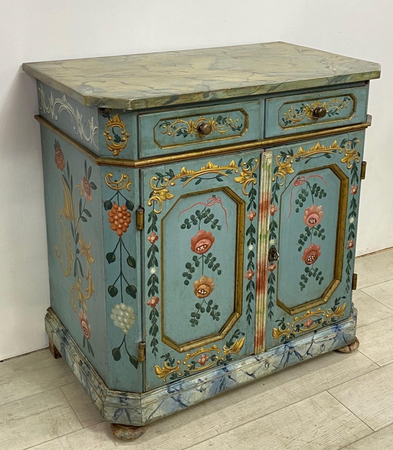 A splendid hand painted cabinet in remarkable original condition. Charming flower motif with painted faux marble top and faux marbling on the molding around the base. Buffet has two drawers above a pair of paneled doors and having a single shelf.