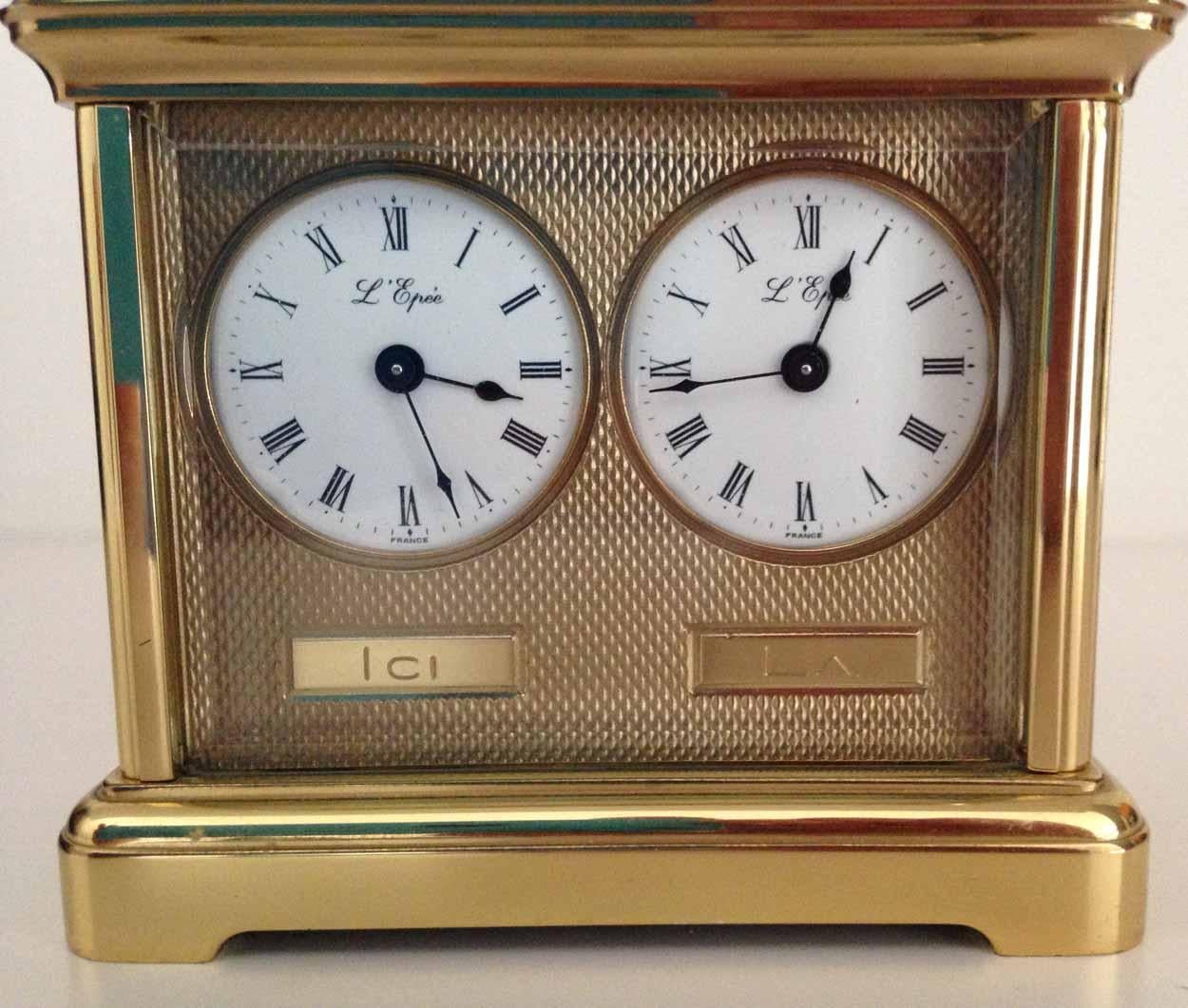 L'Epee Swiss miniature dual timezone carriage clock, circa 1970s.
The white enamel dials with Roman numerals and spade hands, the gilt brass case with glass sides and top, hinged handle

The small size of the clock with dual faces was designed