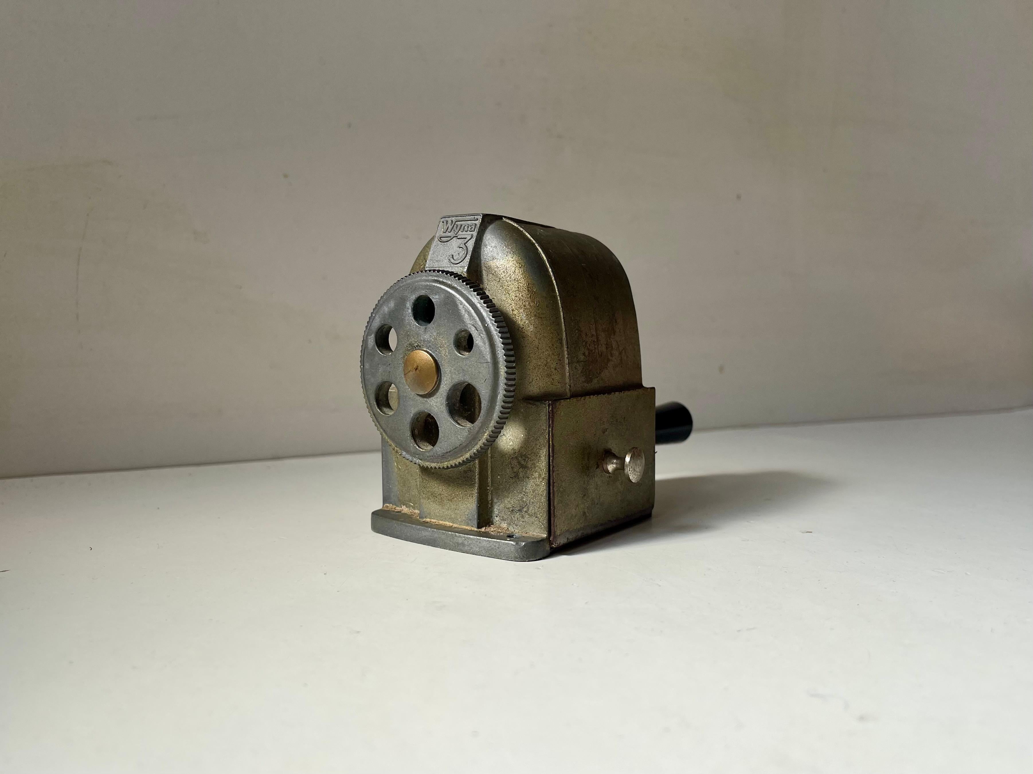 A machine age styled mechanical pencil sharpener made by Wyna in Switzerland during the late 1940s. Designed inspired by the front of a train. Adjustable front and a practical small drawer for the remains. It has patina and is in working order.  