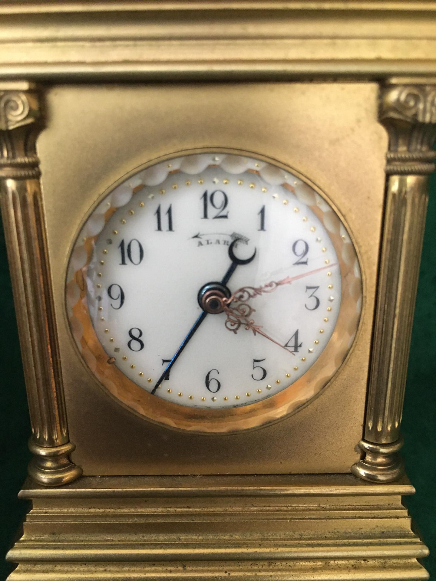 This miniature Swiss carriage clock features a gilded brass pillared case with rectangular top and folding handle over push repeat button, above four solid sides held by fluted columns with Ionic capitals and
hinged rear door. The whole is on a