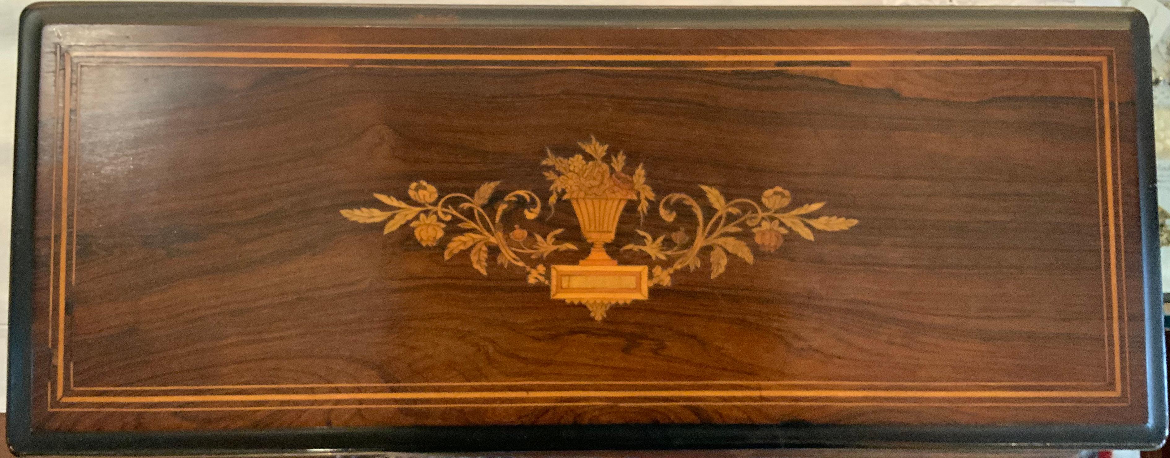 Large Swiss music wood case with details of floral vase marquetry and a string inlaid in the top of the lid. This one has in the back the original tune sheet listing. It has a single cylinder playing eight airs. Inside the wood case there is a
