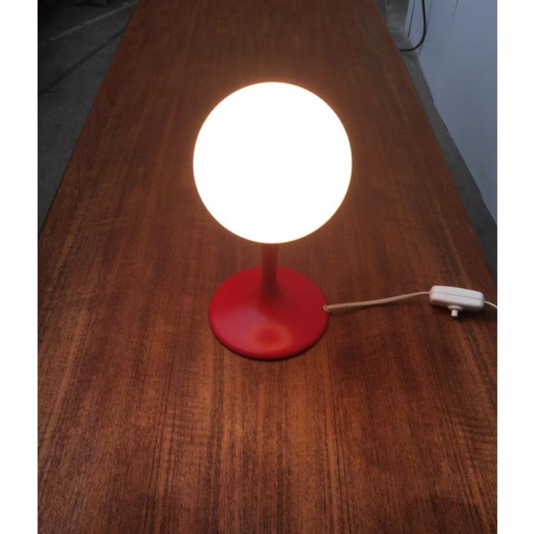 Small table lamp by the Swiss manufacturer Temde to a design by Renee Nele.

Simple table lamp in a distinctive color. An opal glass globe sitting on a elegantly curved, trumpet-shaped foot. The foot is designed in red and goes up harmoniously into