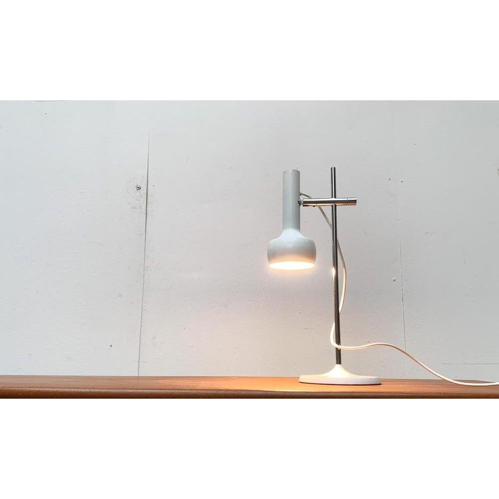 Minimalist table lamp from Swiss Lamps International.

A simple and understated design in white and chrome. The lamp head shows a spotlight shape with a distinctive shade. It can be adjusted in height on the shaft and individually aligned via a