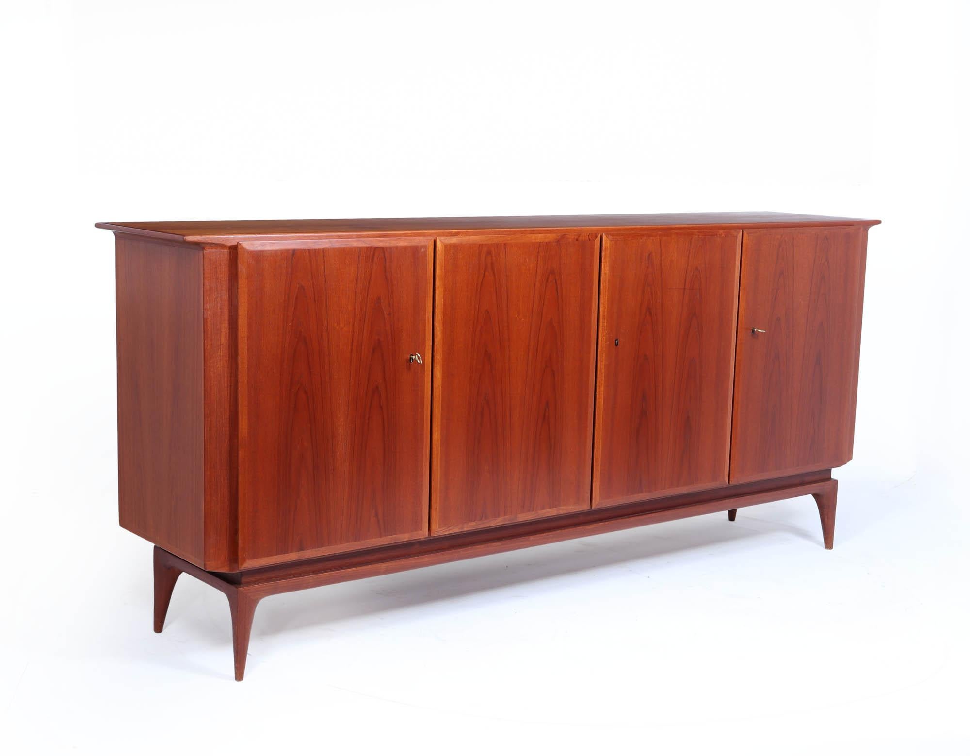 Teak  Credenza
Una credenza di metà secolo prodotta negli anni '60 dai rinomati produttori di mobili Swiss Teak, dotata di quattro ante con serratura e ripiani regolabili e cassetti retrostanti, che poggia su una base molto elegante.

Età: