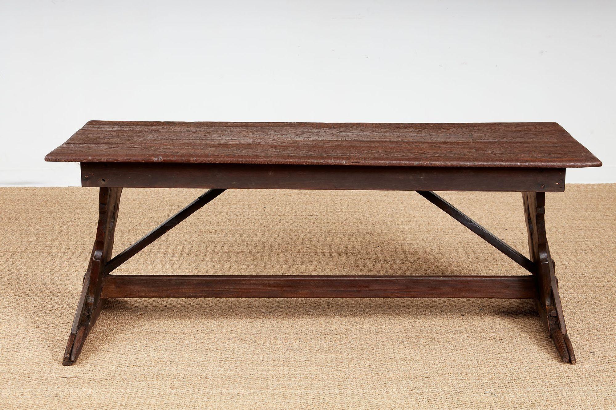 A large Swiss dining table  with a planked top above a straight apron standing on canted and shaped trestle ends joined by a tie bar support.  Notable for its graffiti carvings to the top.  Table dates to the mid 19th century,  while the carvings