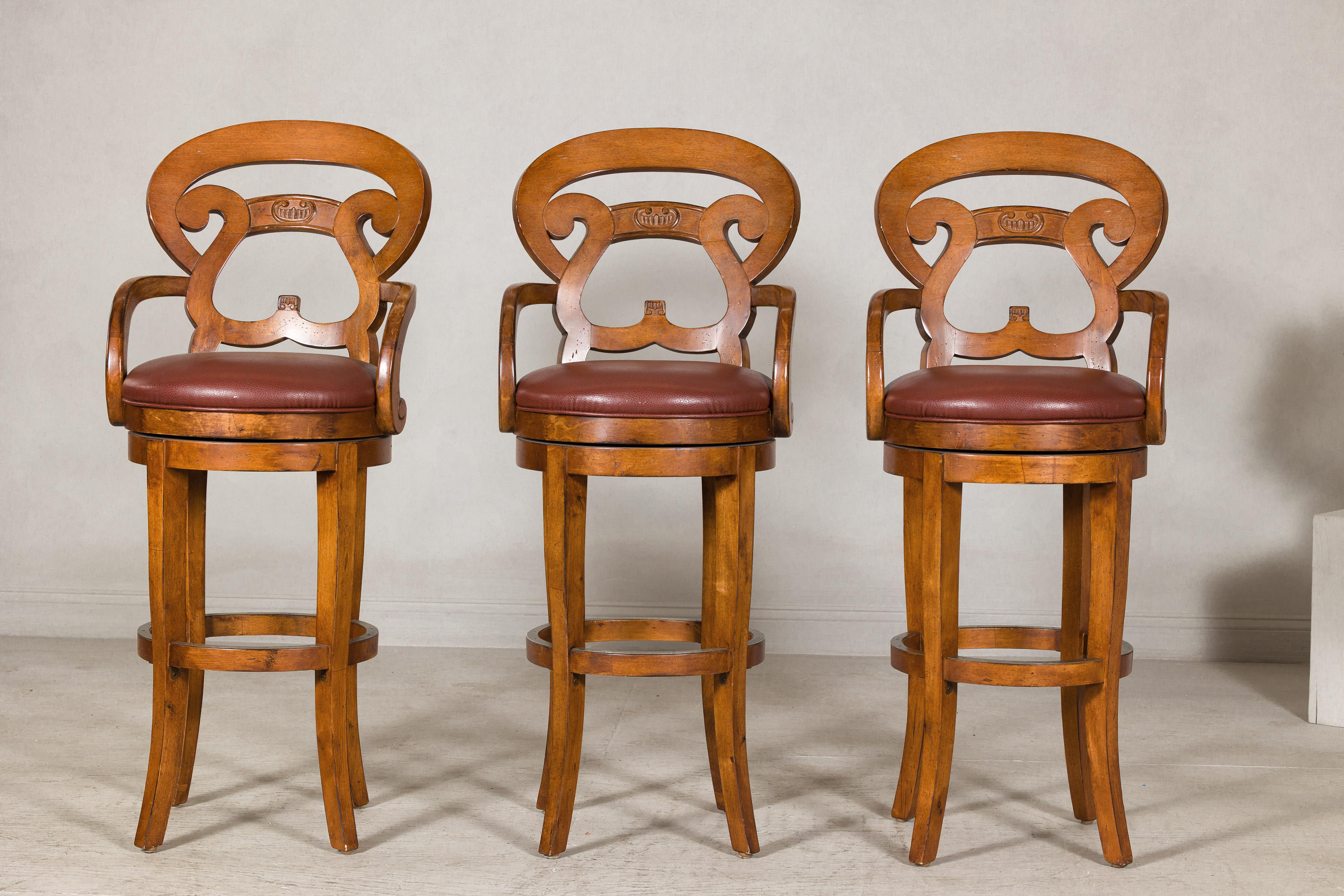 A set of three wooden swivel bar stools with carved backs. Elevate your home bar or kitchen island with this exceptional set of three contemporary swivel bar stools. Crafted with exquisite attention to detail, these stools feature beautifully