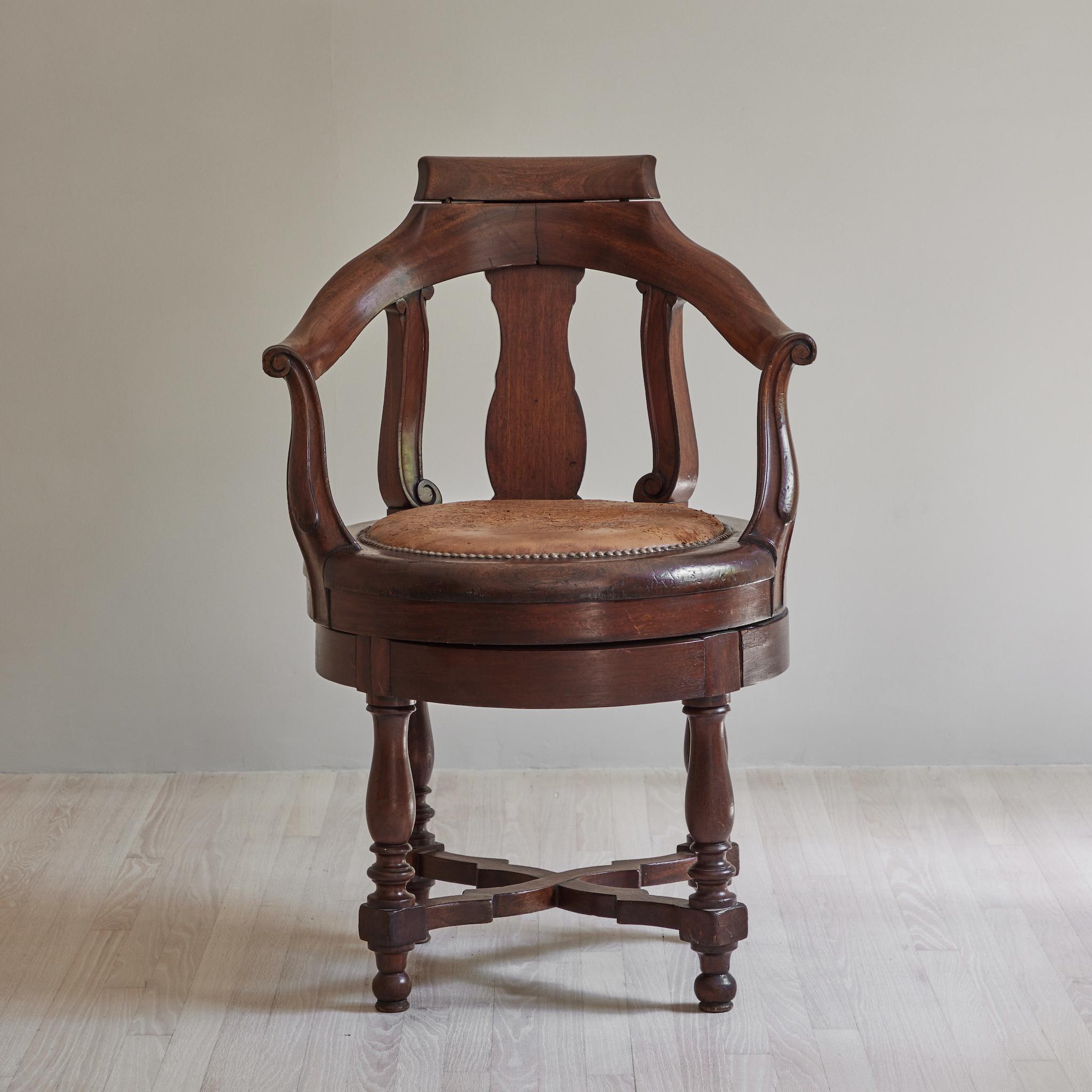 Rare French 19th-century swivel chair with a unique adjustable head rest. Secured with a ring of metal studs, the tawny leather seat complements the rich mahogany wood. Mounted on elongated urn-shaped turned wood legs and with graceful, sloping