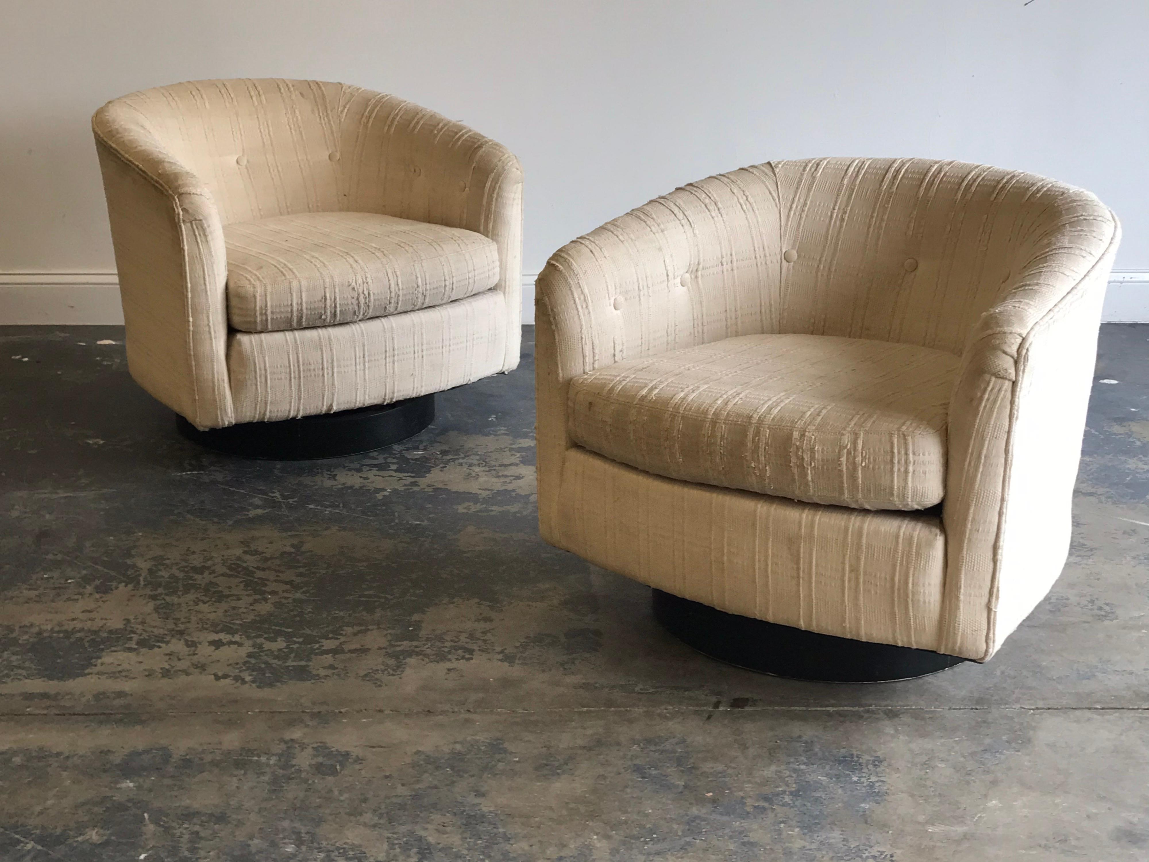 Iconic pair of swivel tub chairs attributed to Milo Baughman. Ebonized wood base supports a tub shaped swivel chair. Swivel mechanism works well. Present tag appears to be from an upholstery shop. New upholstery recommended.
