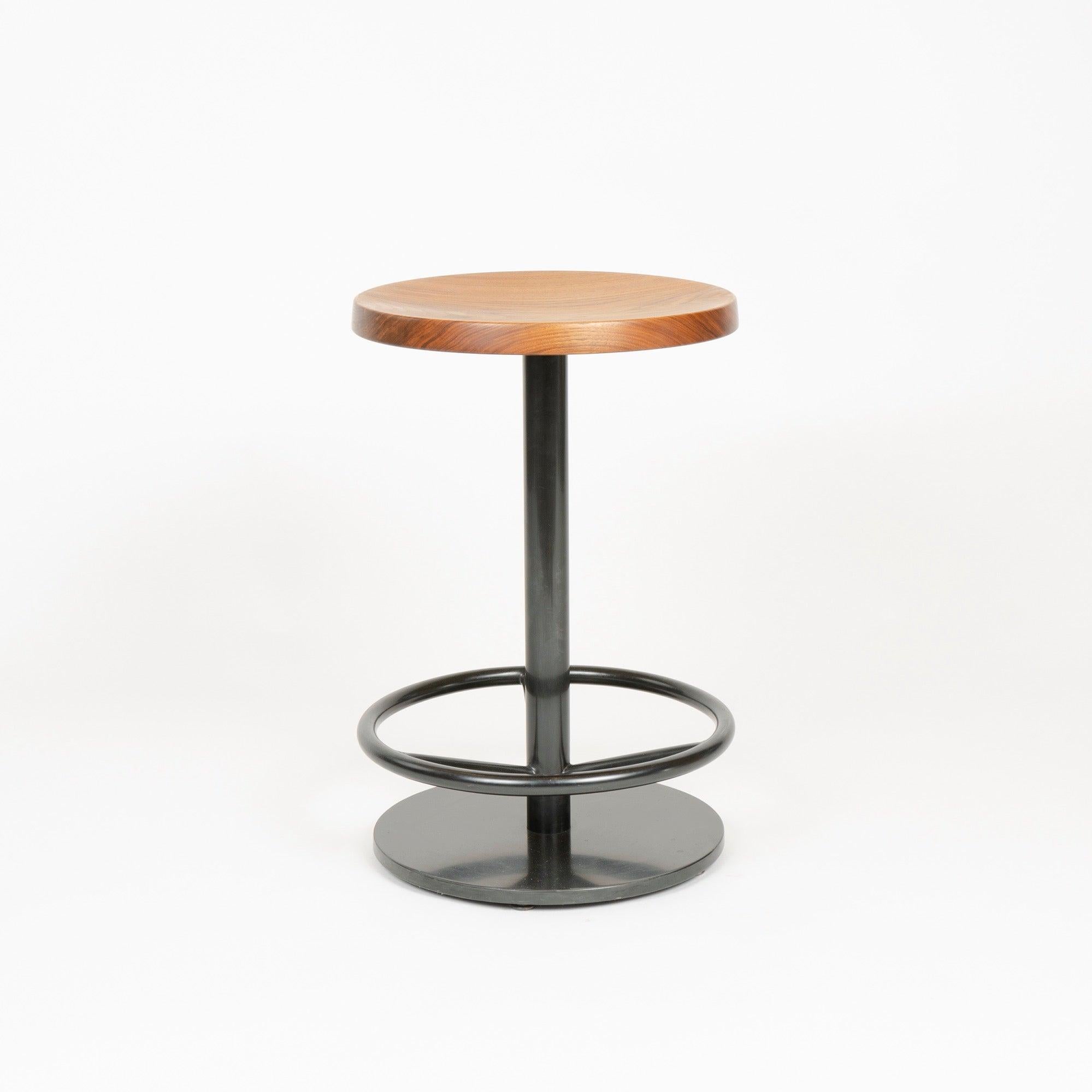 A custom counter stool with a turned walnut seat on a patinated steel base.