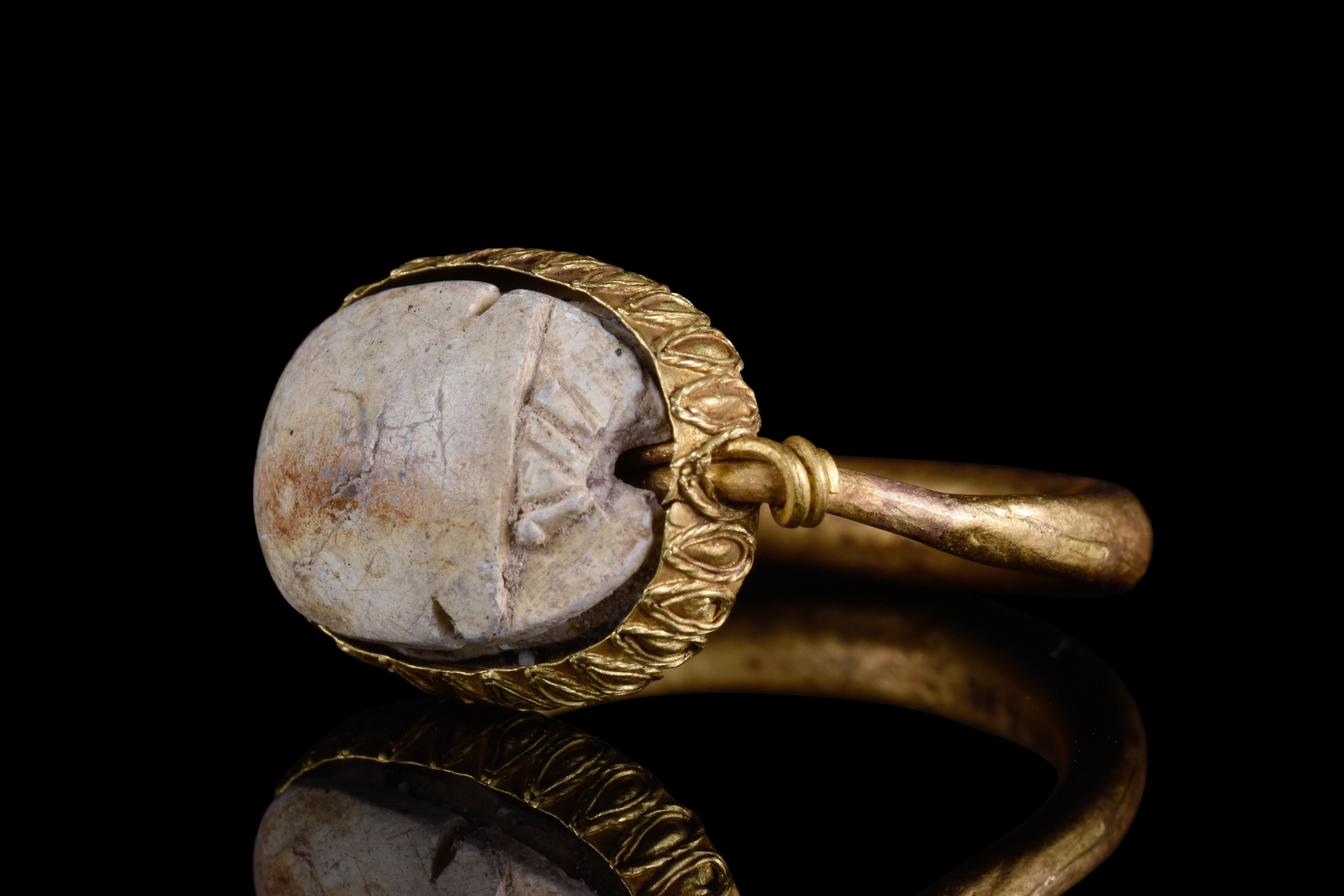 An Egyptian steatite scarab encased in a possibly later, high-karat gold swivel ring. The scarab is a symbol of rebirth and protection and is decorated with six sacred serpents, representing divine authority. The ring has a simple D-shaped design