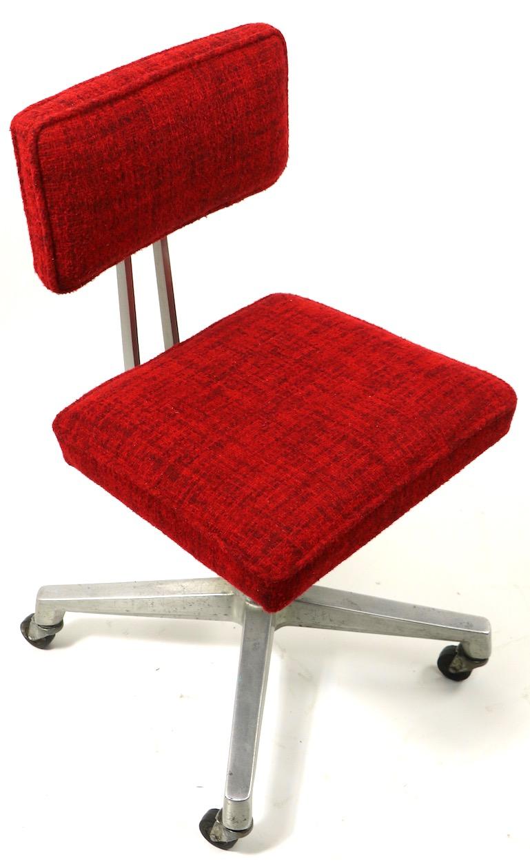Chic and stylish architectural design swivel office desk chair, having a solid cast aluminum frame with textured red fabric upholstered seat and back. The back support and backrest both tilt to adjust position, the chair also swivels on its base,