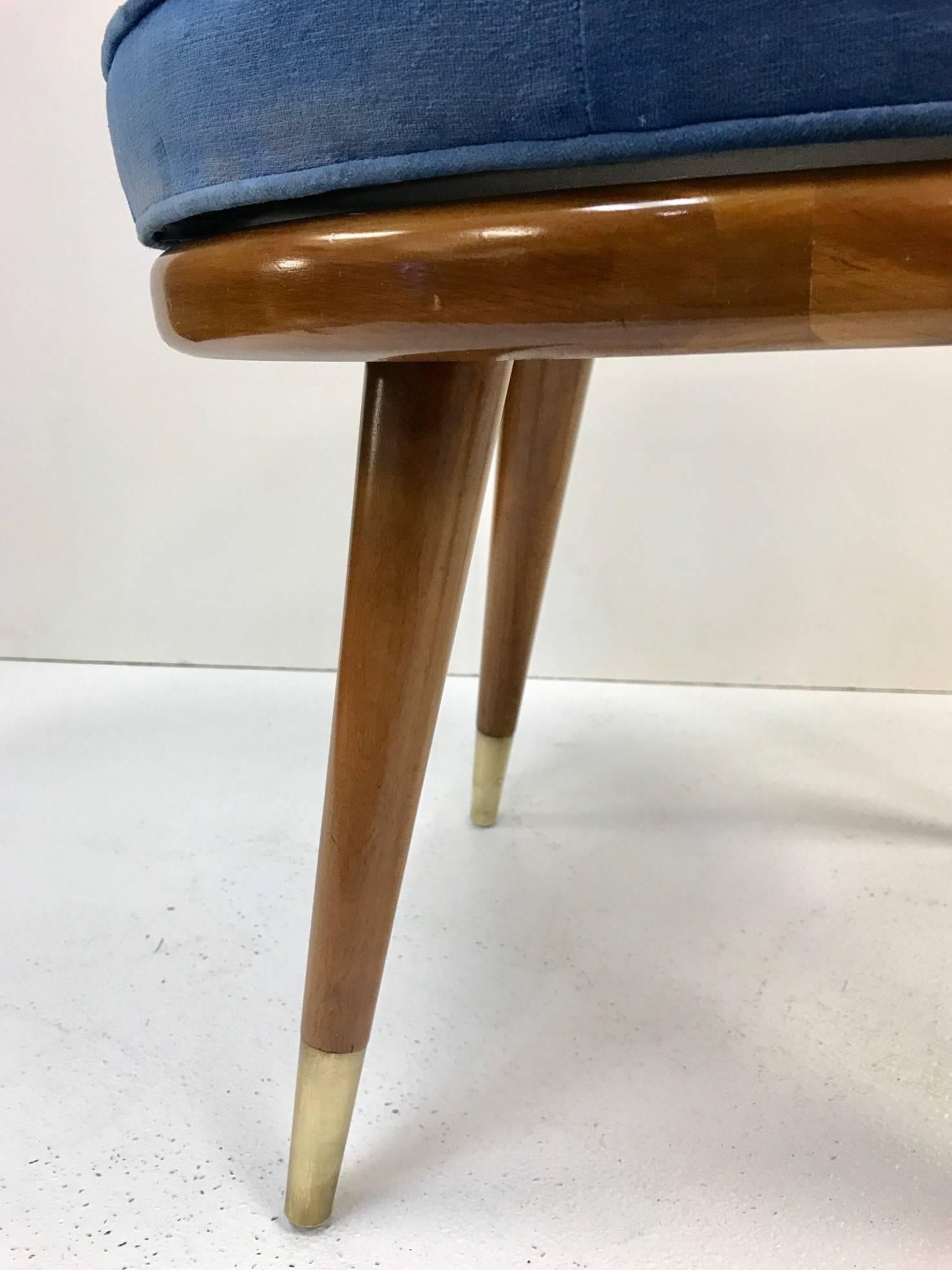 Swivel stool style of Robsjohn-Gibbings. The stool has the original blue velvet upholstered seat, wood frame with brass sabots. Mid Century Modern.