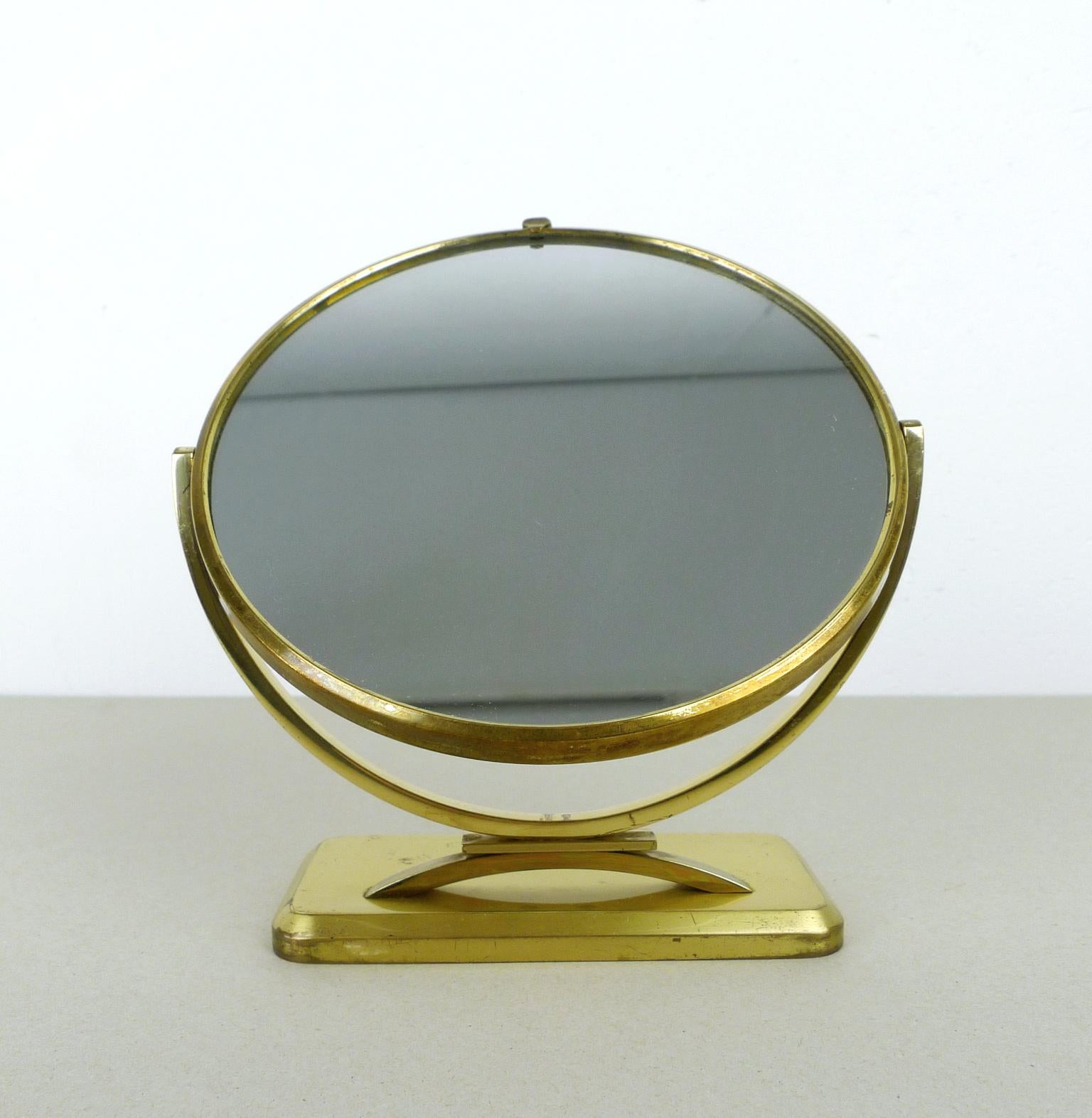 Small round table mirror with brass stand and handle from the 1950s. The mirror can be rotated around a central axis. The back has green polka dot pattern behind a domed glass cover. It is in good original condition.