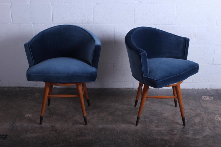 A pair of swiveling vanity stools/chairs by Edward Wormley for Dunbar. Reupholstered in blue velvet with maple legs and brass sabots. Priced and sold individually.