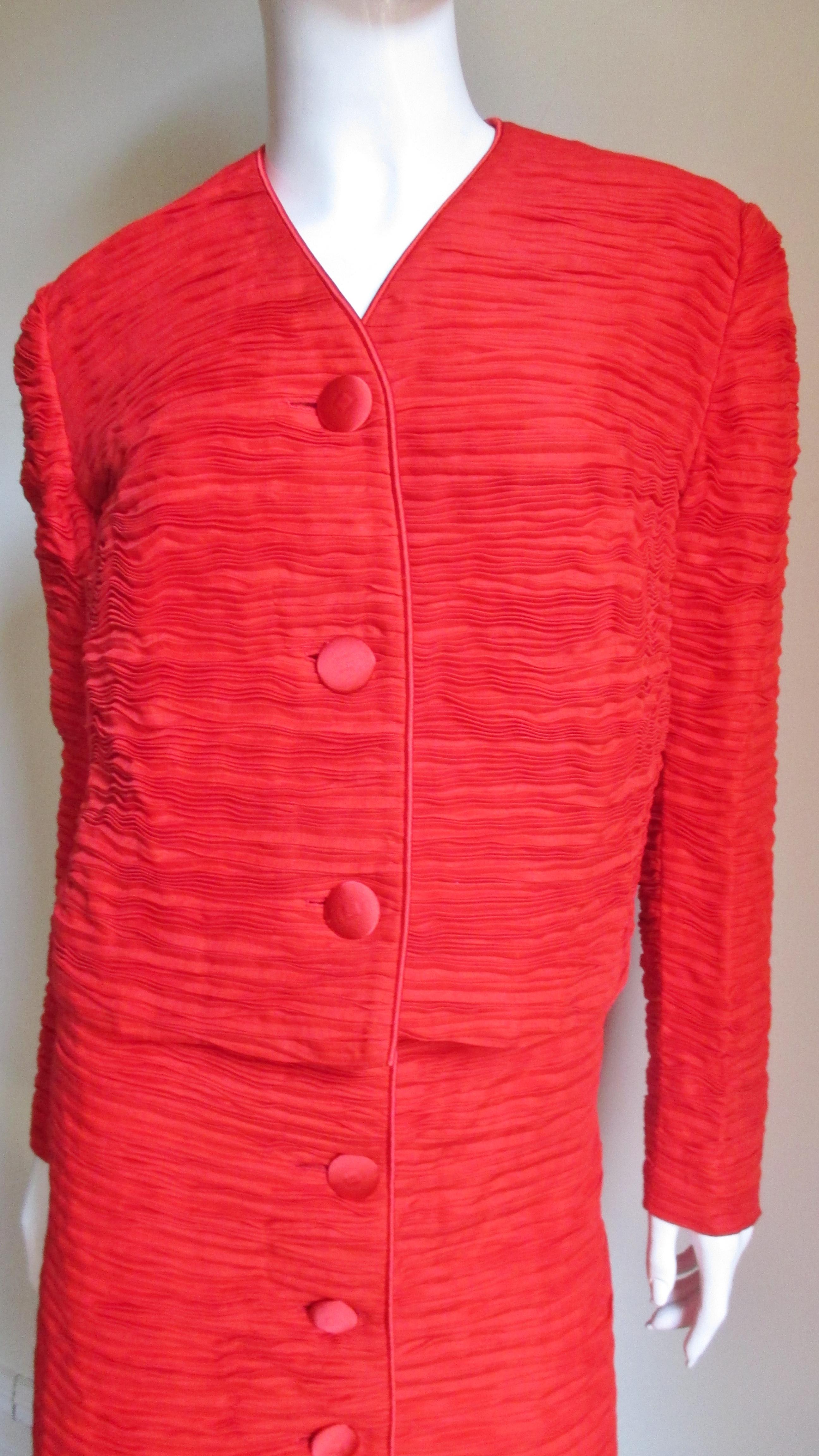 An incredible red suit in intricately pleated fine linen made famous by Sybil Connolly. The jacket closes in front with matching silk buttons, bound buttonholes with matching silk piping around the V neckline and along the center front.  The A line
