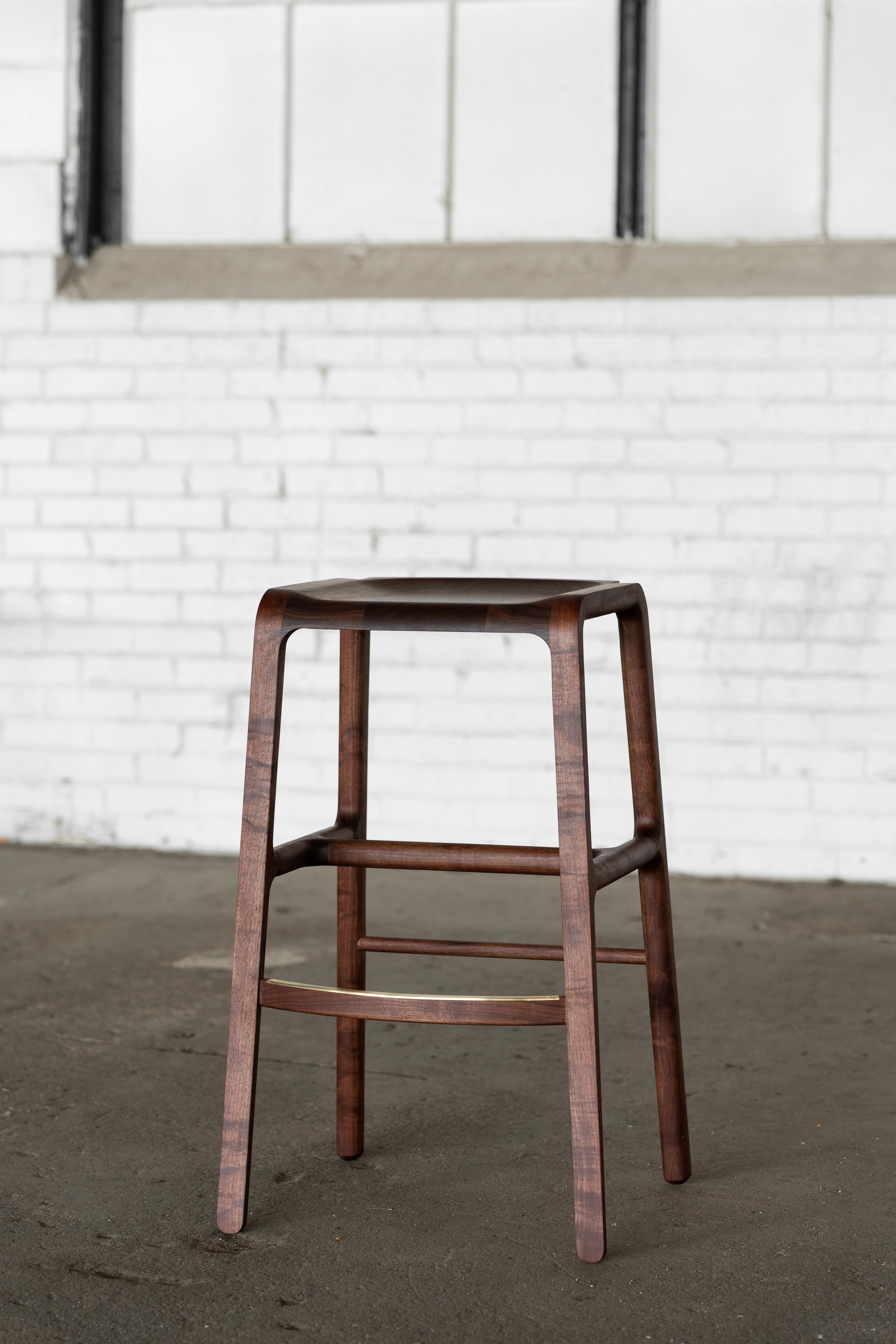 Cette pièce est un tabouret tout en bois avec de subtils détails en laiton.  Notre objectif était de créer une forme moderne unique qui mette en valeur les détails du bois dur naturel tout en faisant écho au charme intemporel de nos chaises Estrada