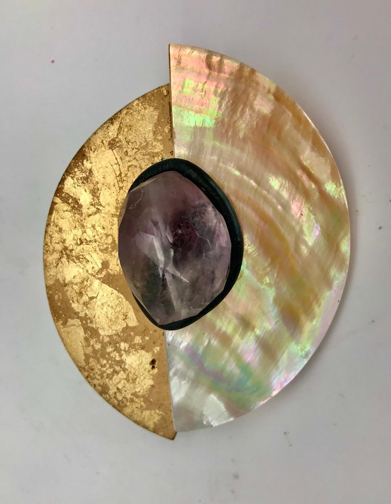  Brooch white/gold Mother of Pearl with Amethyst ;consists of two half circles arranged in an elypse like design lower one having 24 carat gold leaf applied on the surface. The center accent is 1.5 long large faceted Amethyst
framed in rubber tube.
