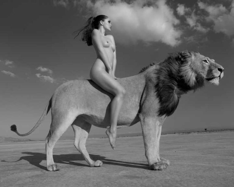 Sylvie Blum Black and White Photograph - Angela rides the lion -  portrait of a female nude riding a lion in the desert