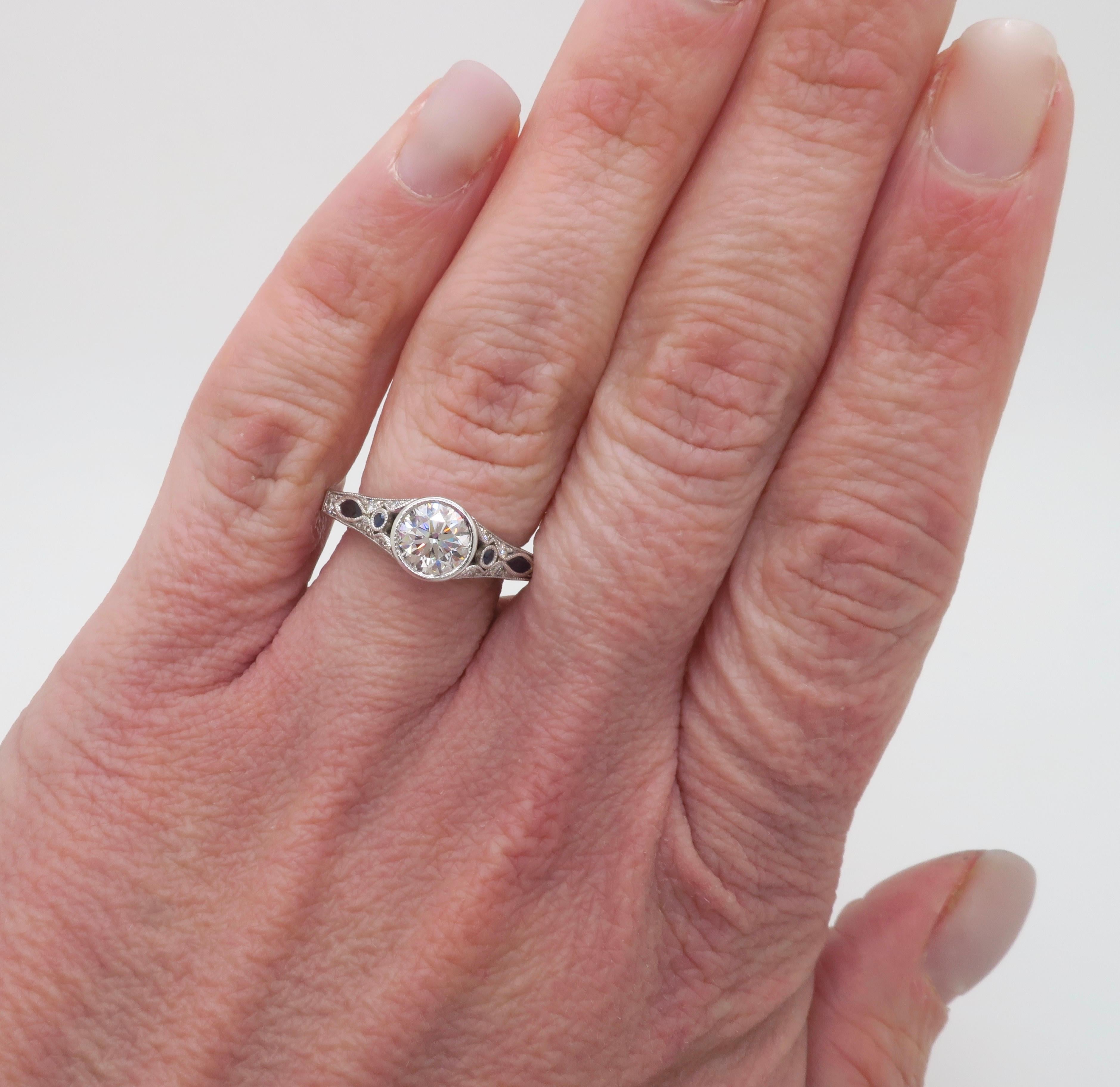 Stunning Sylvie ring crafted in 18k white gold with a bezel set GIA certified Diamond in the center and blue sapphire accents. 

Center Diamond Carat Weight: .90CT Earth Mined
Center Diamond Cut: Round Brilliant Cut 
Center Diamond Color: G
Center