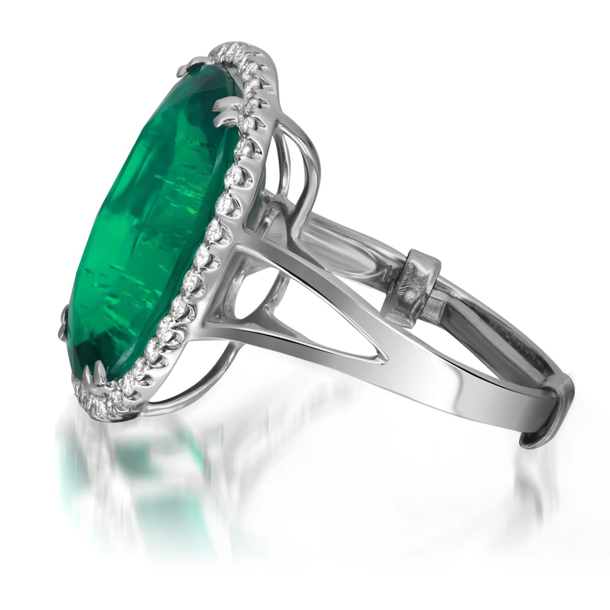 This beautiful oval cut synthetic green emerald and diamond cocktail ring is crafted in fine 18k white gold. An excellent oval shaped synthetic emerald weighs approx. 14.00 carats approximately flanked with a halo of tiny round brilliant cut