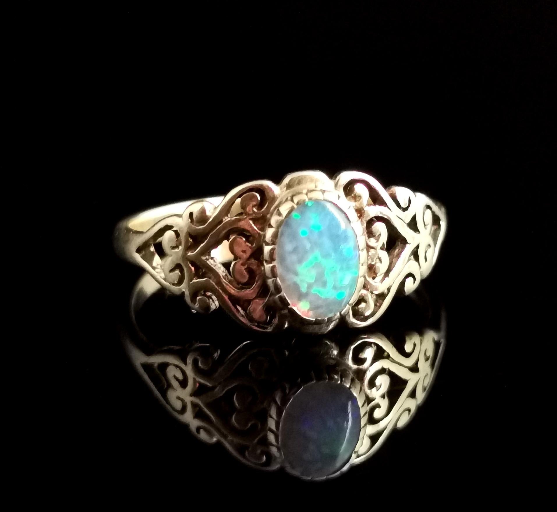 Ein hübscher Kleiderring aus 9kt Gelbgold mit synthetischem oder simuliertem Opal.

Er hat einen hellen regenbogenfarbenen Cabochon mit blauem Grund in der Mitte und dekorative durchbrochene Schultern mit einem Herzmotiv.

Ein hübscher Ring,