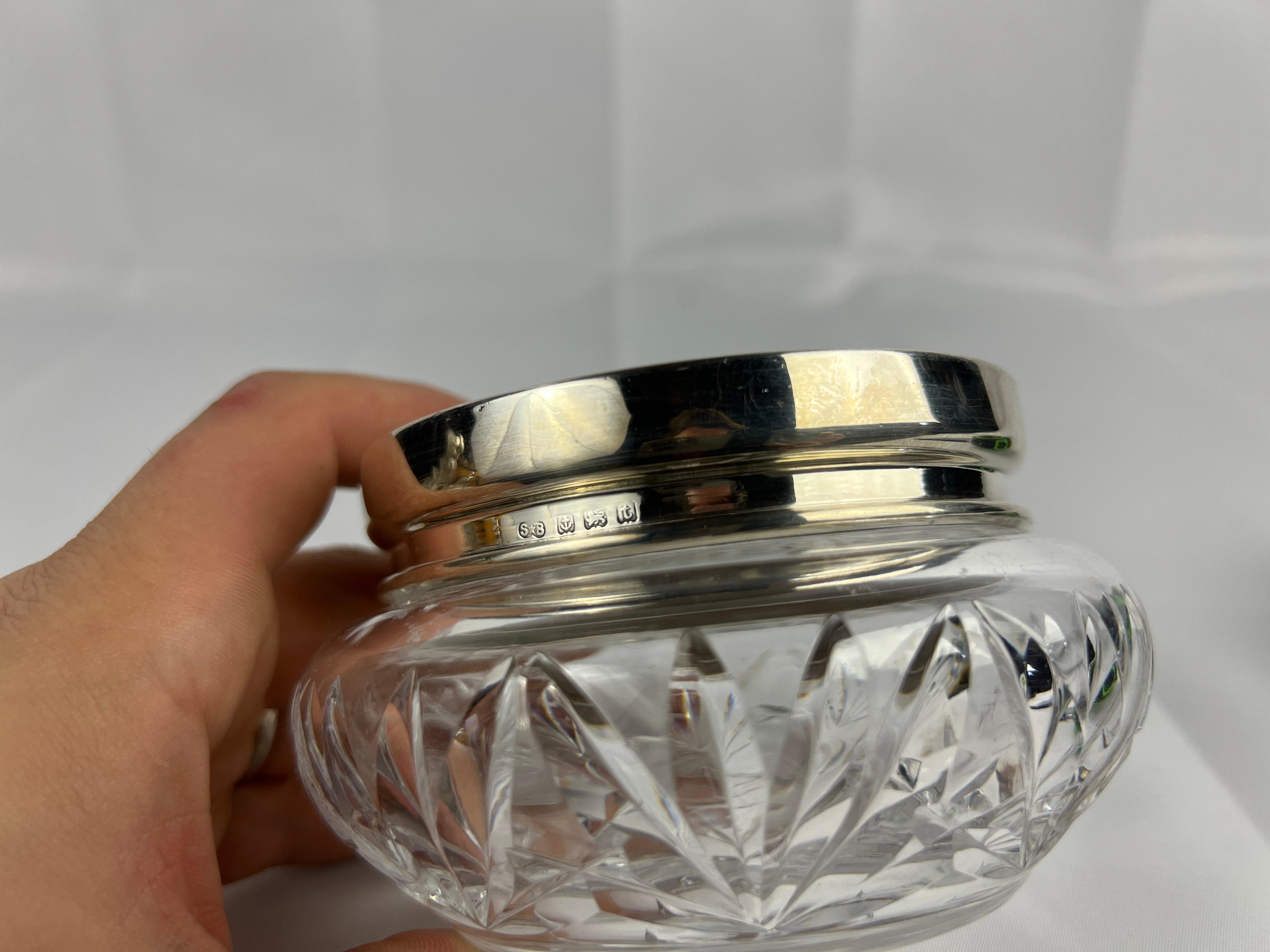 Esta exquisita jarra de tocador, elaborada por los renombrados plateros de Birmingham Synyer & Beddoes, es un asombroso ejemplo del diseño inglés de principios del siglo XX. Fechada en 1918, la jarra presenta un cuerpo de cristal bellamente tallado,