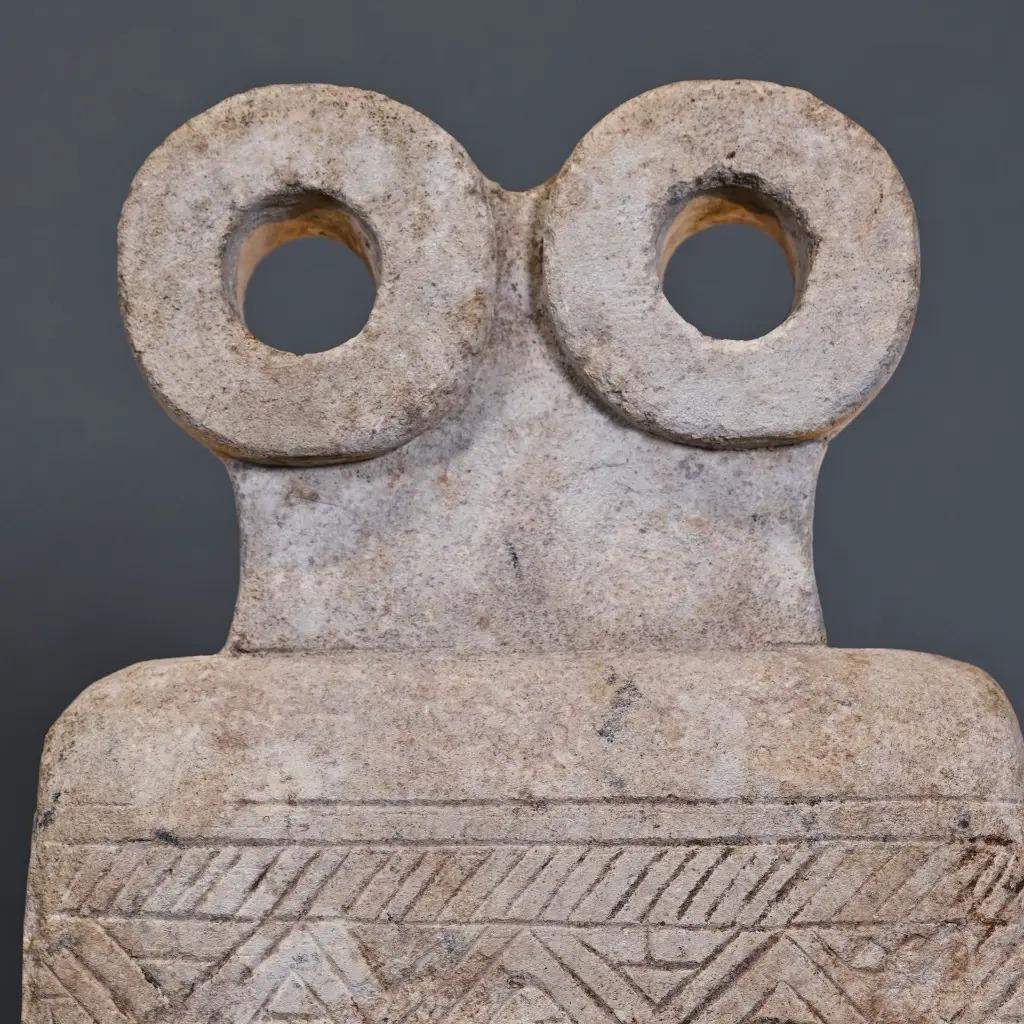 This exquisite Syrian idol in sandstone captures the abstract elegance of ancient Mesopotamian religious art. Hand-carved and carefully patinated, it reflects the symbolic eyes and looped motifs of original votive figures, once used as offerings or