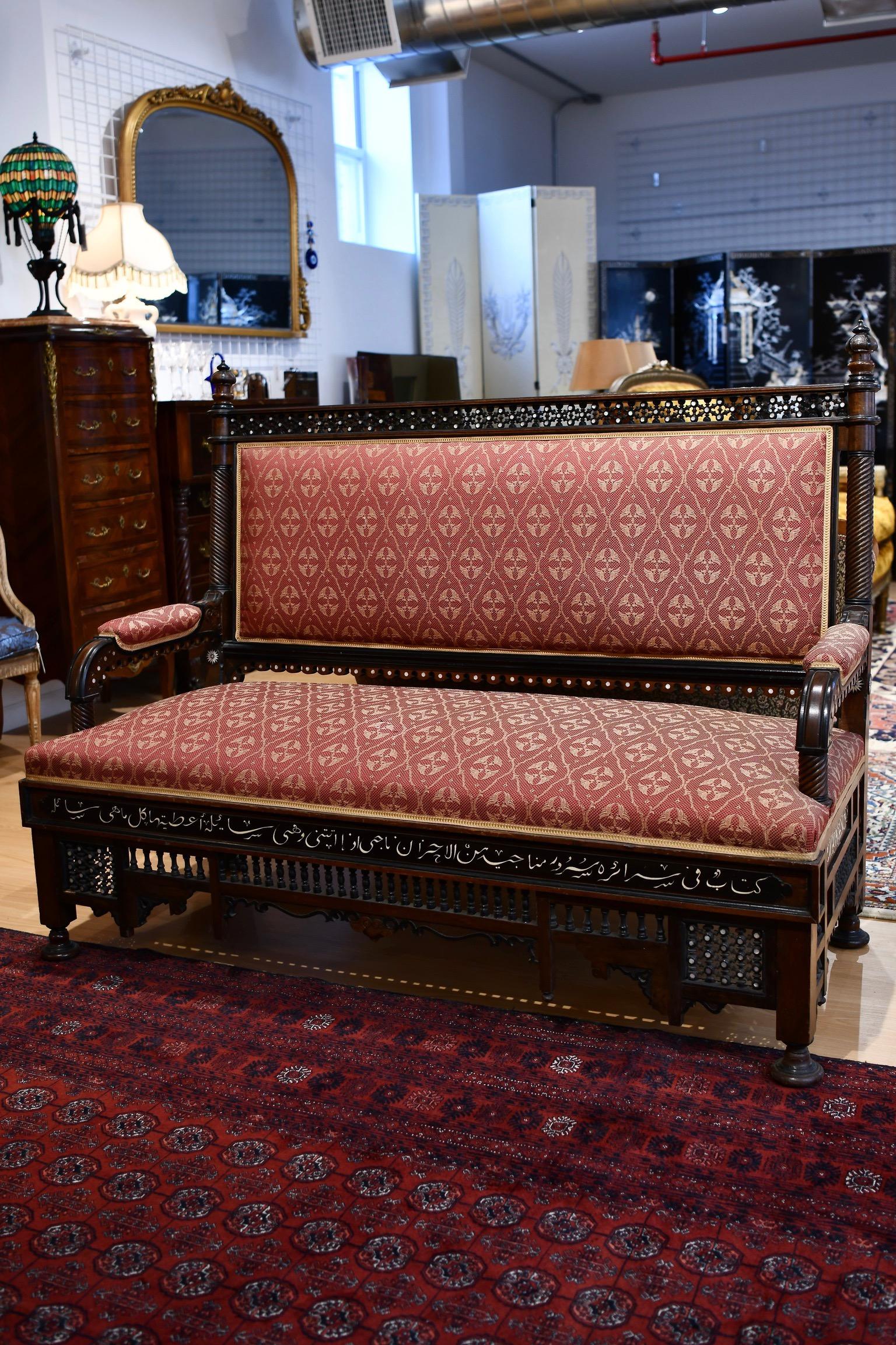 Syrian sofa circa 1900 with mother of pearl details, including Arabic calligraphy and motifs throughout, intricately carved woodwork, and red floral upholstery. Minor imperfection to upholstery but in overall very good condition. Dimensions: 42