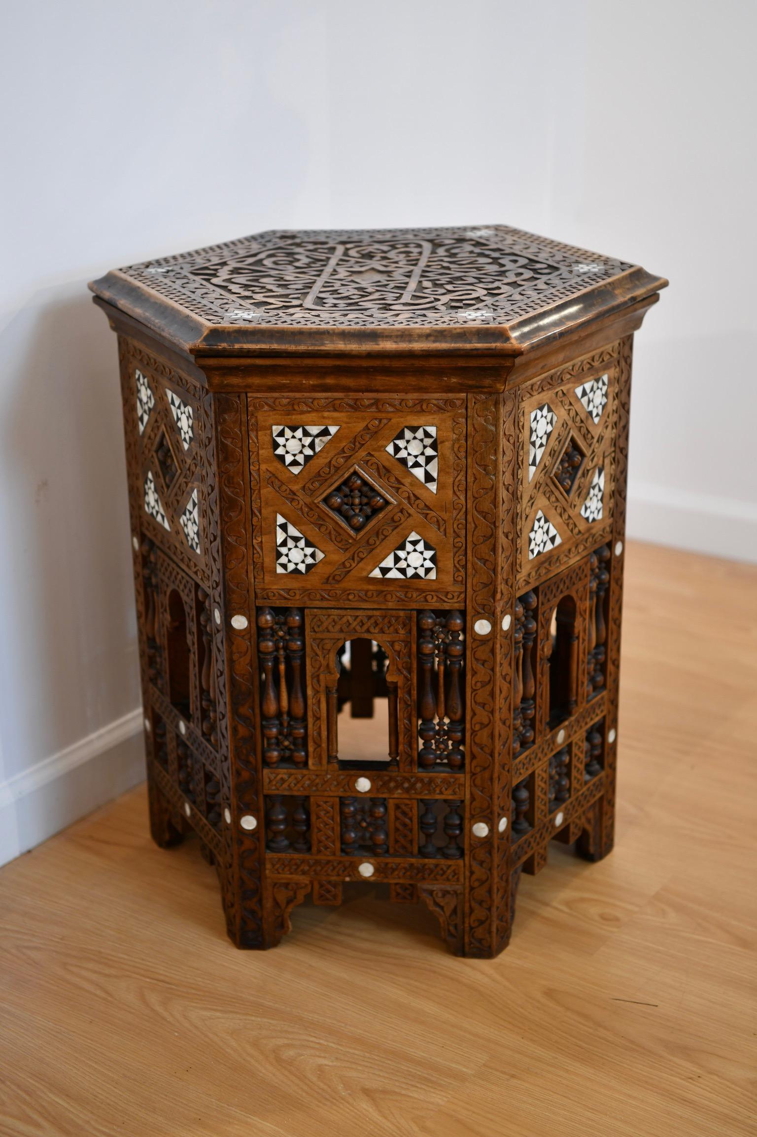 Profusely carved hexagon form Syrian table with mother of pearl inlay throughout and carved Arabic calligraphy to top. Tabouret opens to reveal storage compartment. In overall very good condition.Dimensions: 24.5