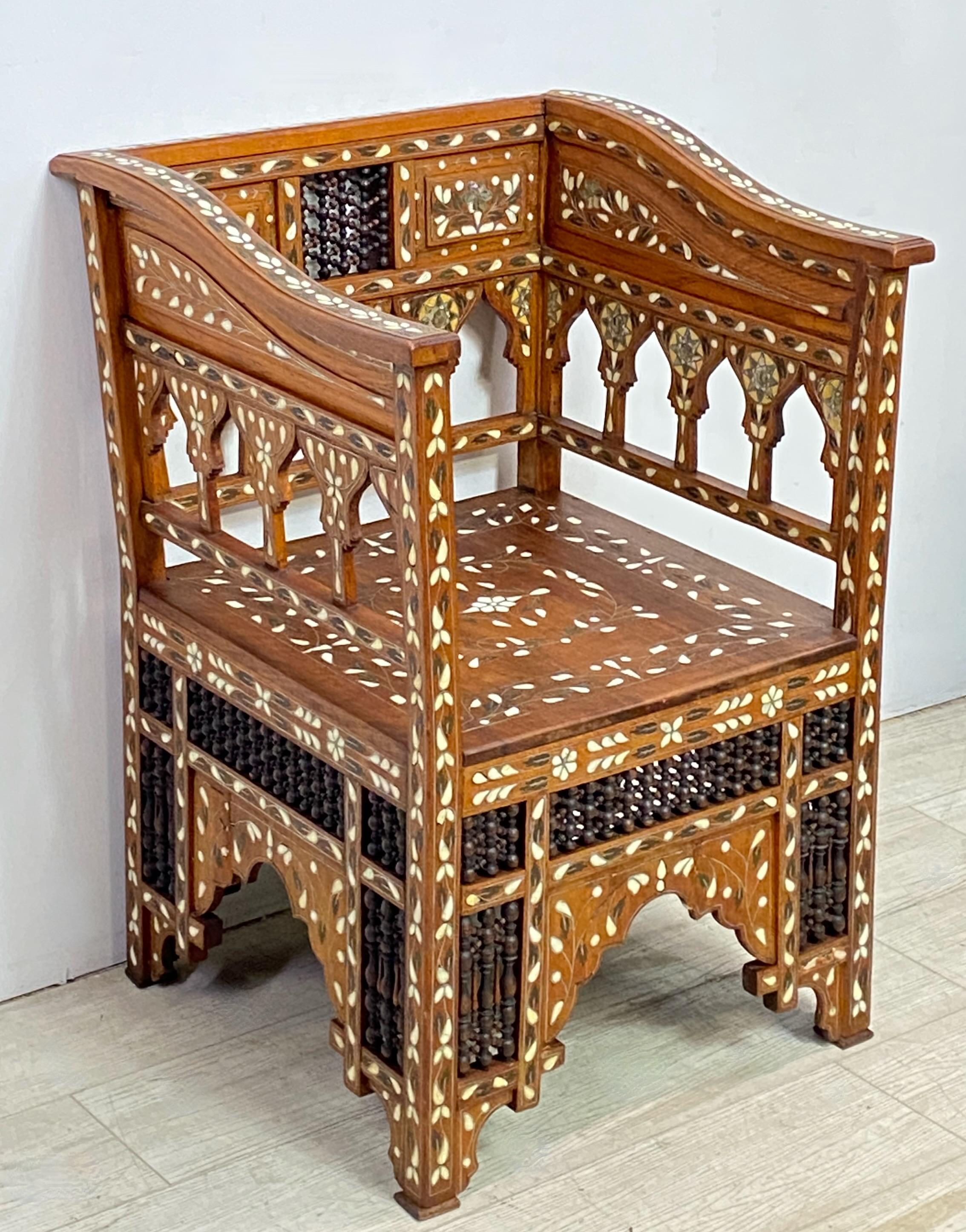 A highly decorative example of a Late 19th / Early 20th Century hand carved Syrian Moorish style armchair with velvet and appliqué cushion. Walnut with hand turned fretwork and elaborate inlay detail of brass, bone, and mother of pearl.
Sturdy and