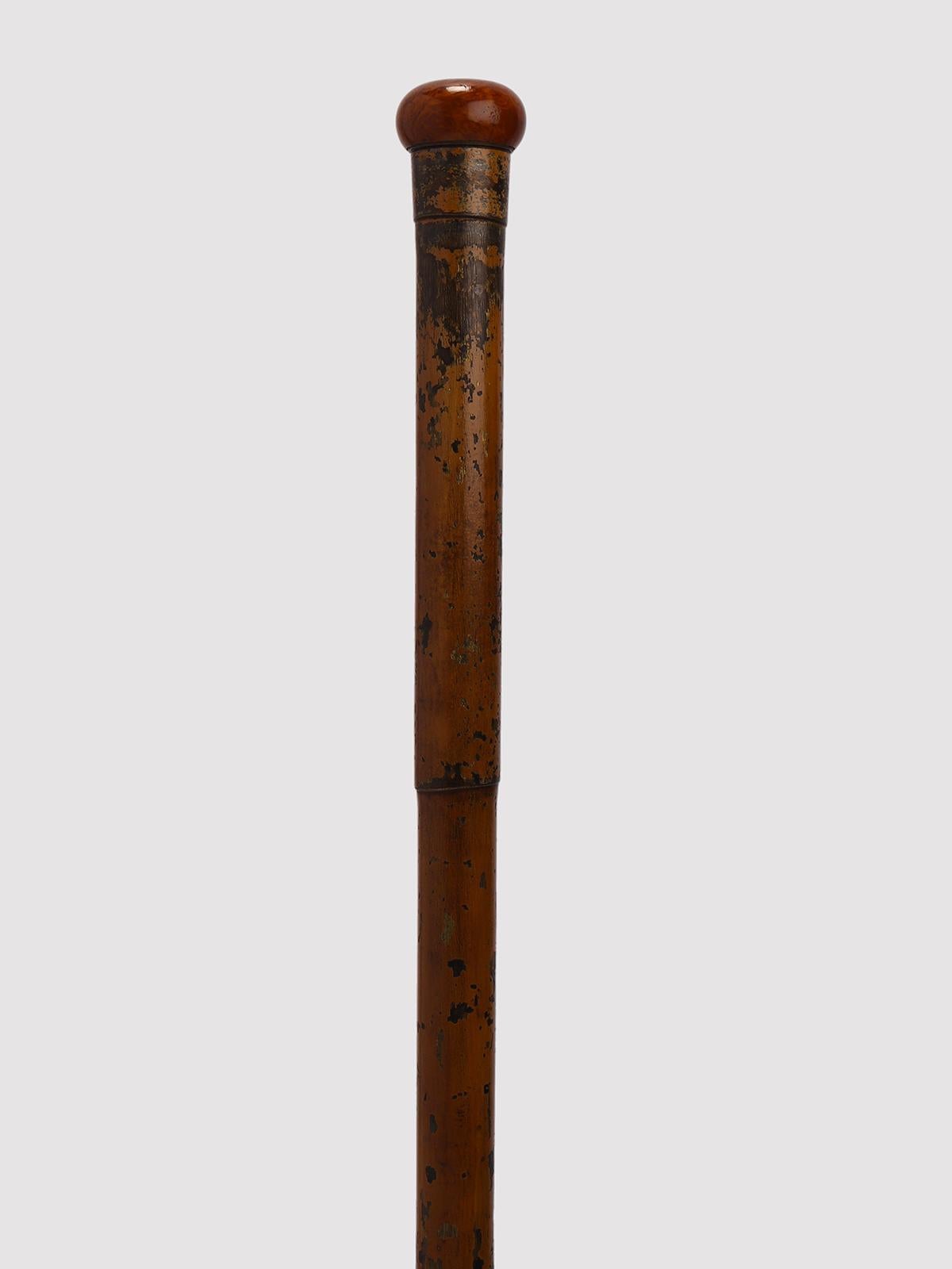 Bastone Gadget-System. La punta è in ferro e ottone, alta e decorata da una serie di cerchi sottili. L'asta è realizzata interamente in ottone verniciato e costruita in modo da emulare una canna di bambù. La verniciatura dell'intero barile ha