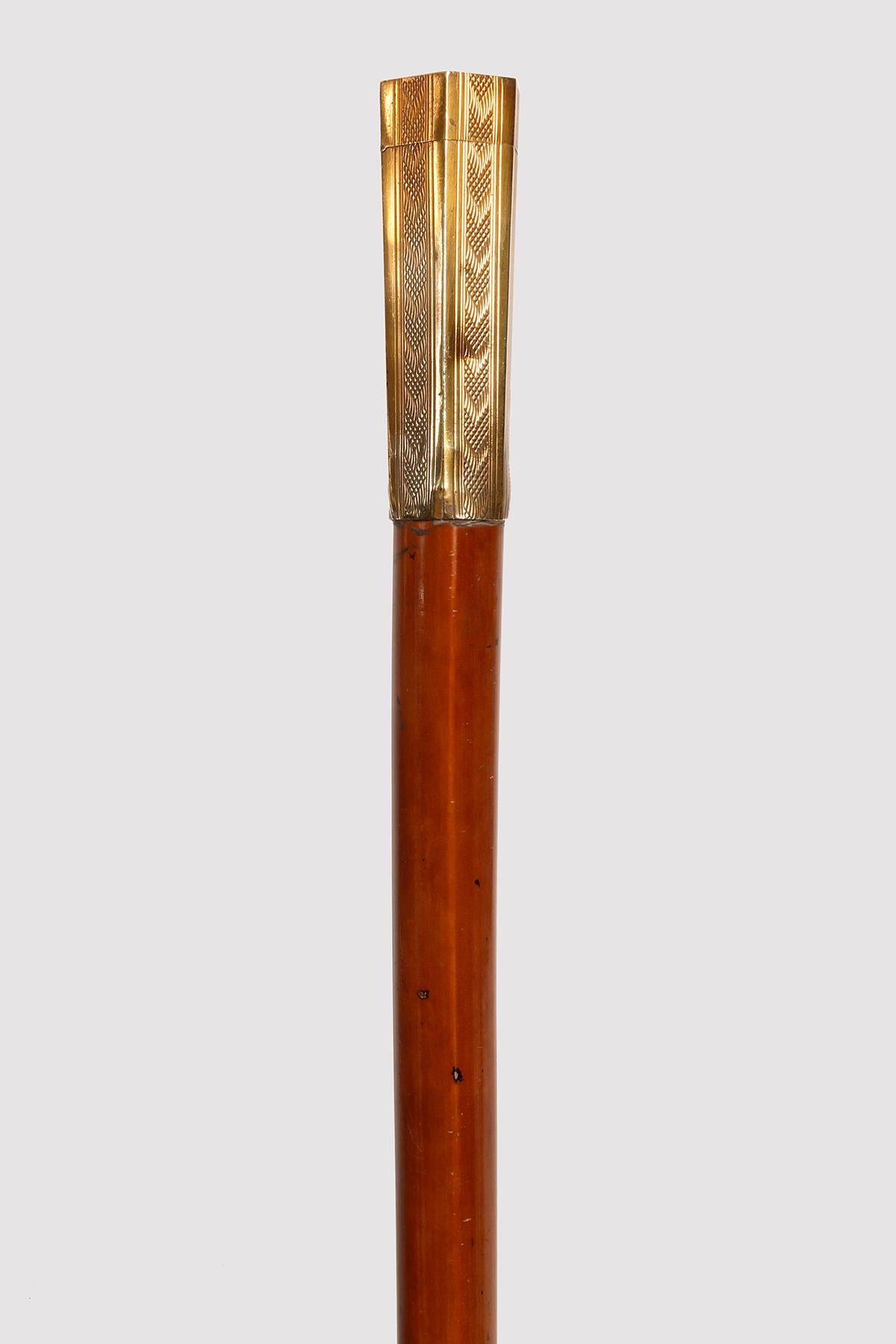 System walking stick with black cow horn tip. The barrel is made of light malacca. The handle is made of gilded brass, with an hexagonal section engraved with geometric motifs. The finial is hinged and opens to reveal a wick inside. France, around