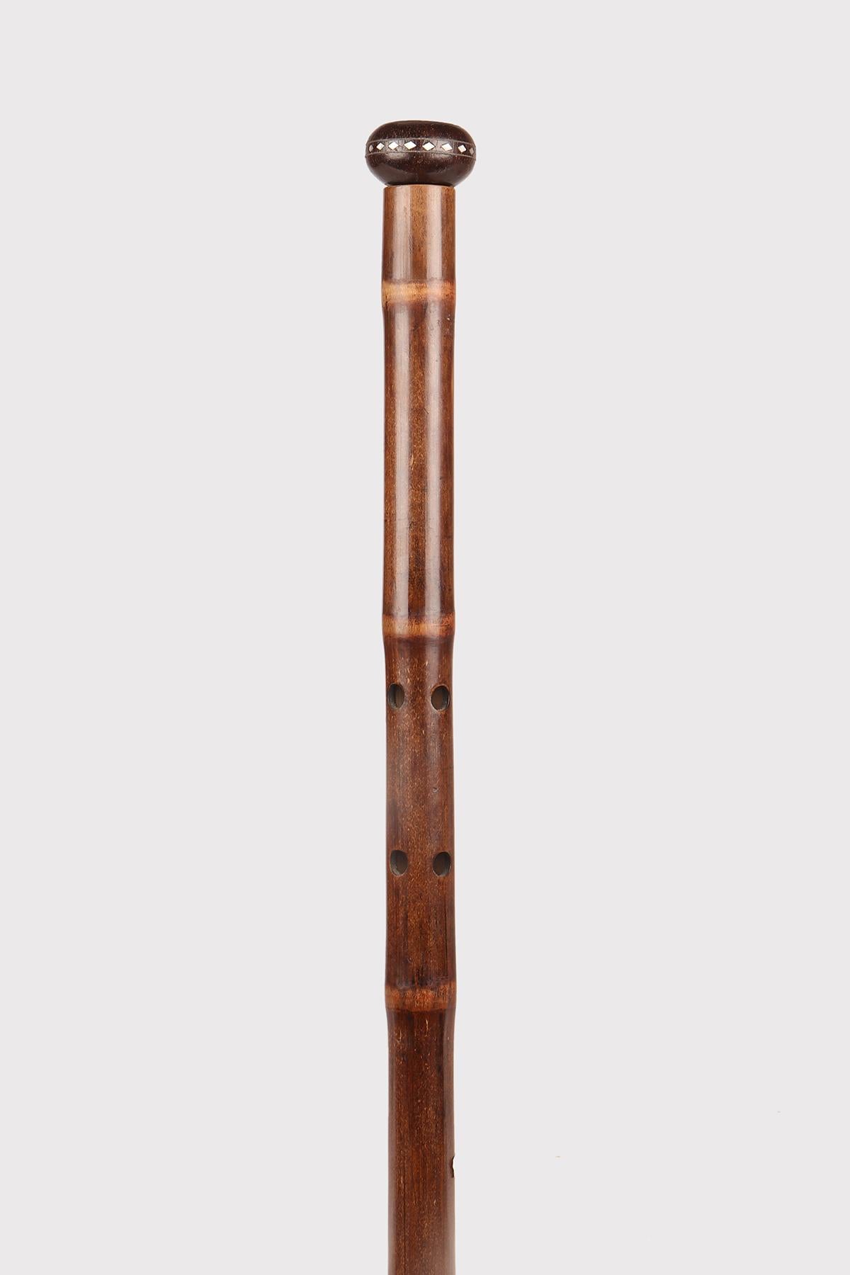 System walking: stick with the function of a musical instrument, the flute. Bamboo wood cane. Wooden and mother-of-pearl knob carved and engraved with E M monogram, brass and iron ferrule. Inside the shell and cable, and the holes allow you to play