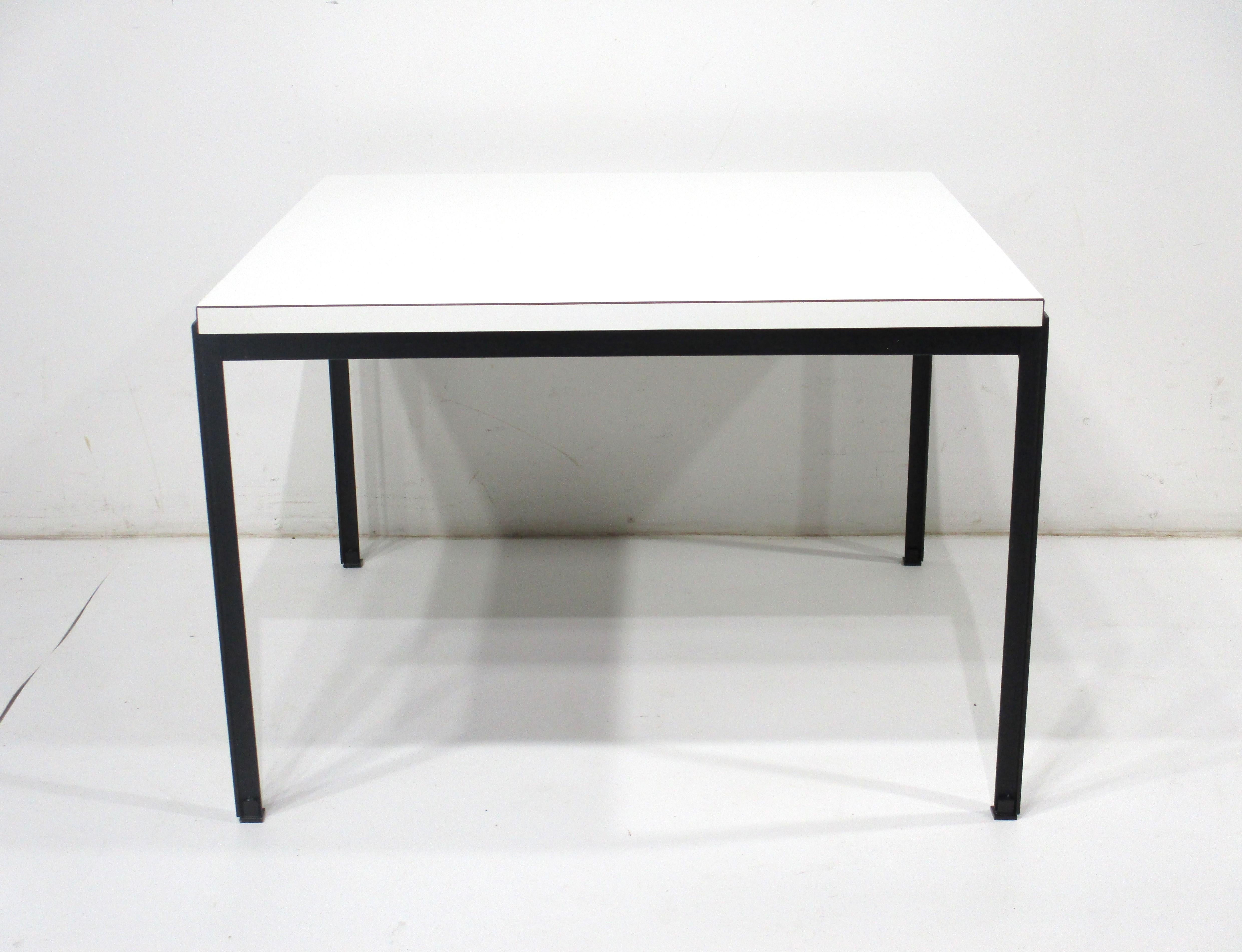 A very nice simple side table with satin black T angled steel frame and with a white Laminate top . A very early production piece having the big fabric label to the bottom from Knoll Associates and designed by Florence Knoll , from the original
