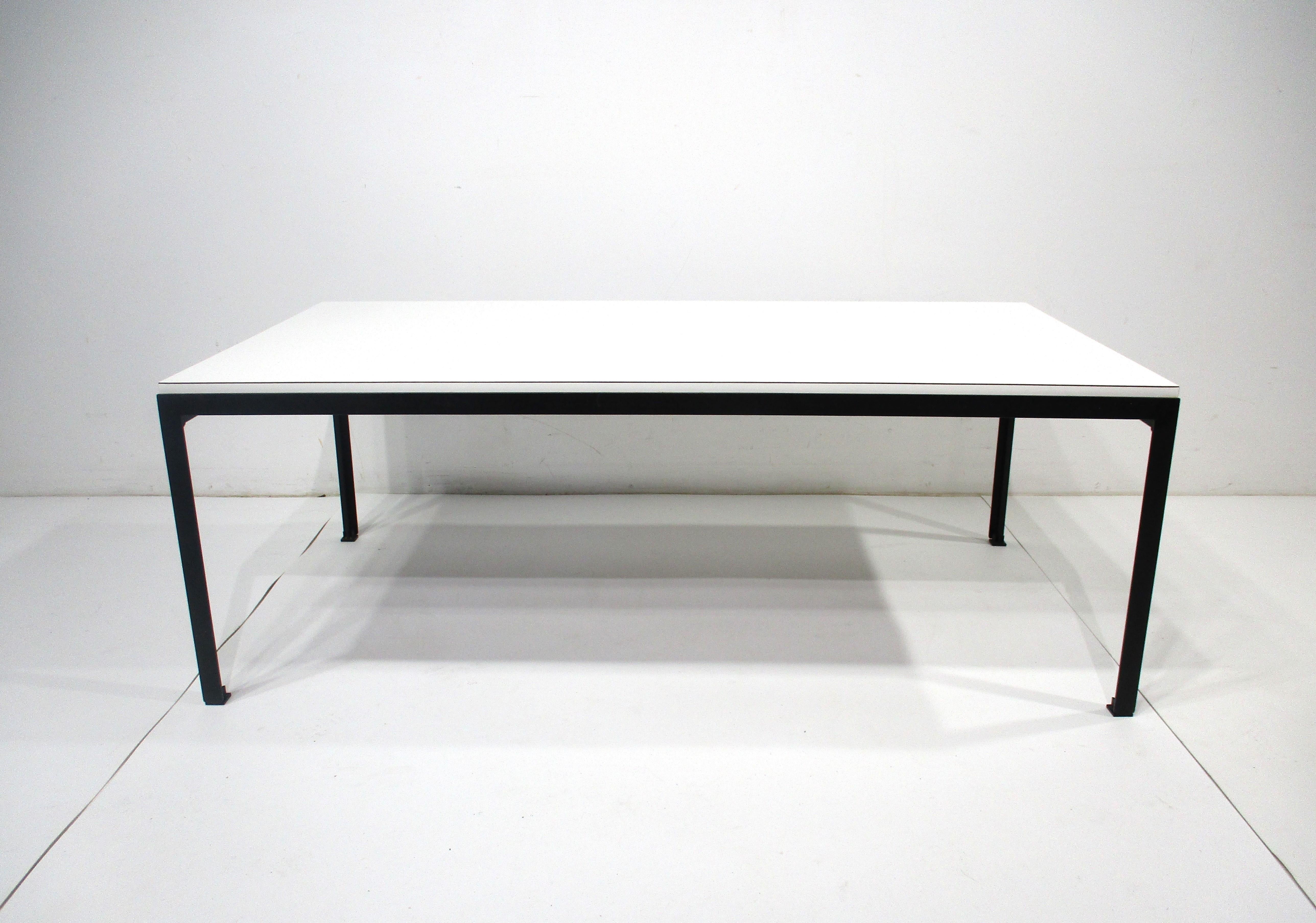 A very early T- Angle satin black metal based coffee table with a white Laminate top . The base has a nice architectural feel with black plastic T formed foot pads to protect your floors . The first series table has the large cloth big K label