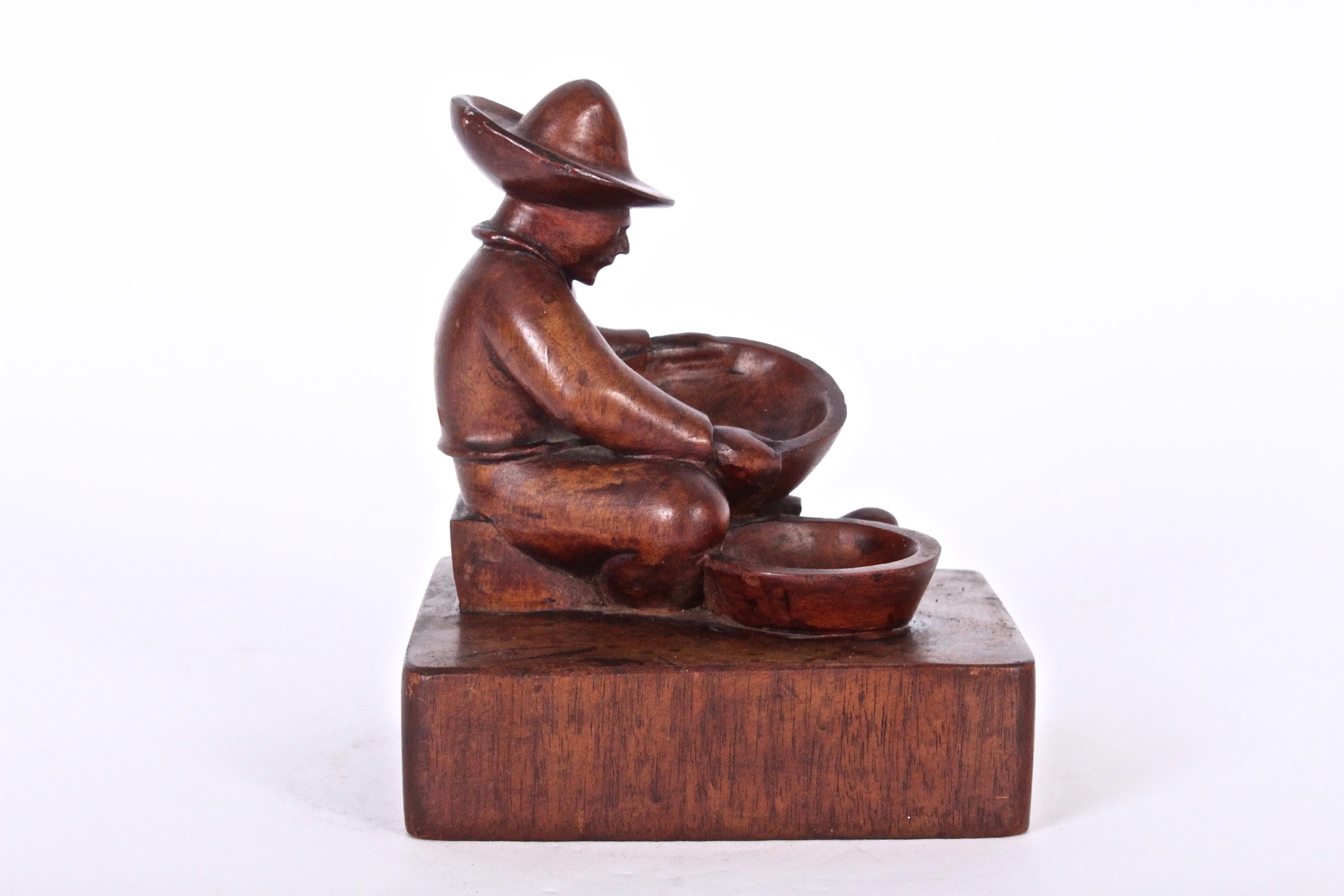 Early 20th century Mexican hand carved Folk Art figurative small mahogany jewelry bowl by T. D. Somes. Featuring a hand carved seated man with hat & two bowls elevated on a square wood base. Sanded. Polished. Finished. Hand-sculpted. Primitive.