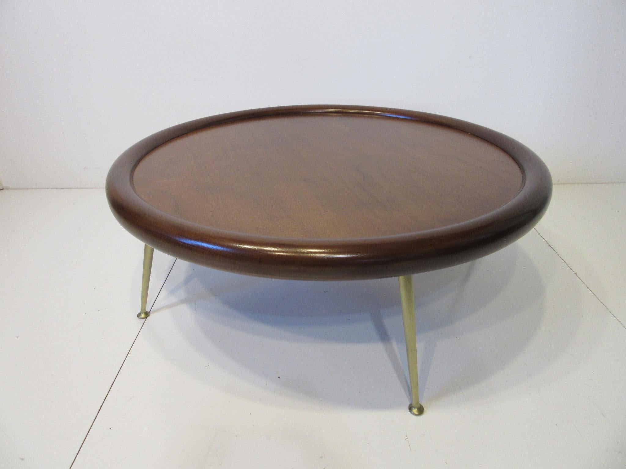 A rare well crafted and beautiful round coffee table with lighter toned walnut inner surface and darker toned walnut bull nose edge sitting on cast polished brass legs. Retains the manufactures label to the bottom by the Widdicomb Furniture Company