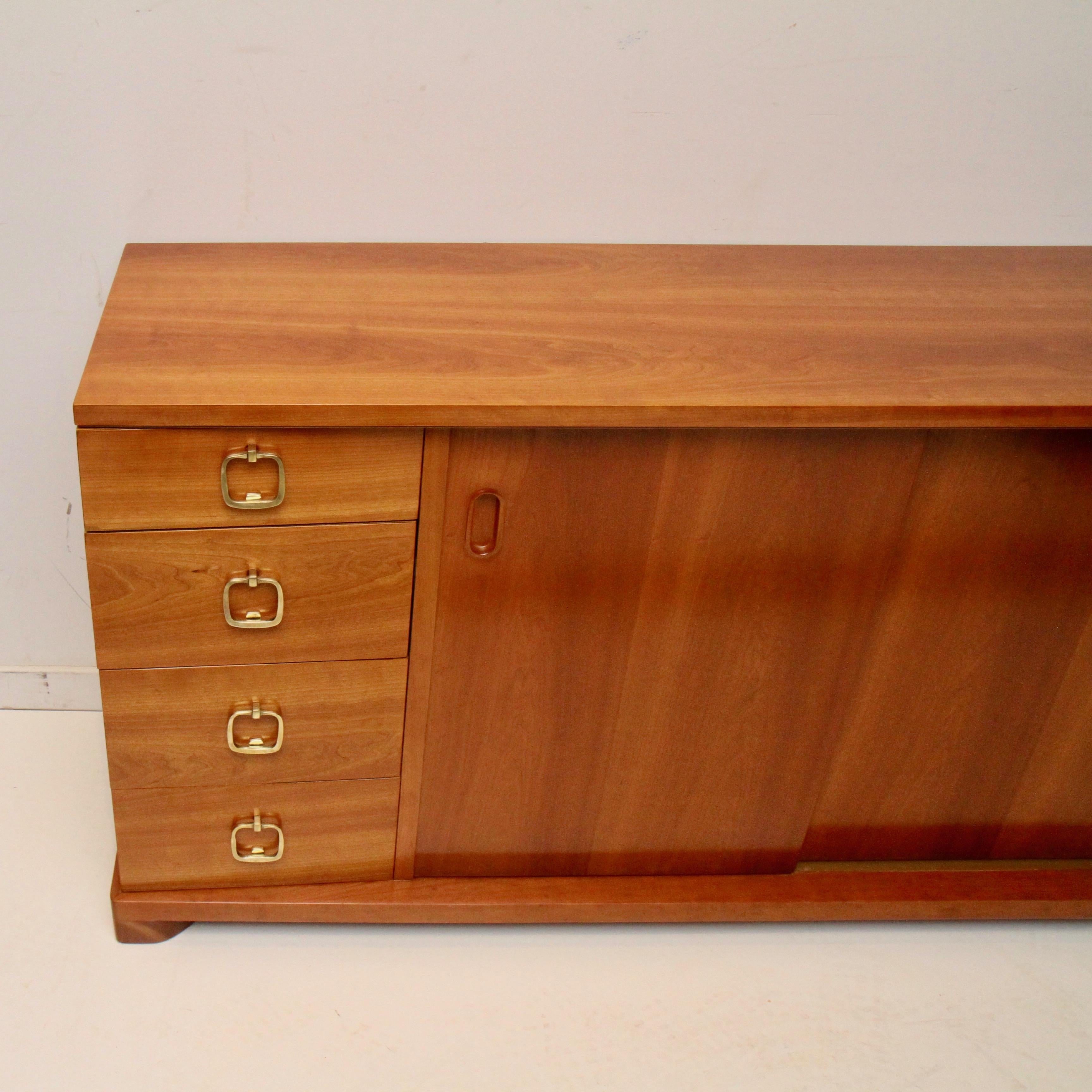 Freshly refinished after 50+ years with its original owners, this old-school, well-built masterpiece by Robsjohn-Gibbings for John Widdicomb is good to go for another 50. Solid brass pulls open 8 side drawers, while sliding doors hide another wider